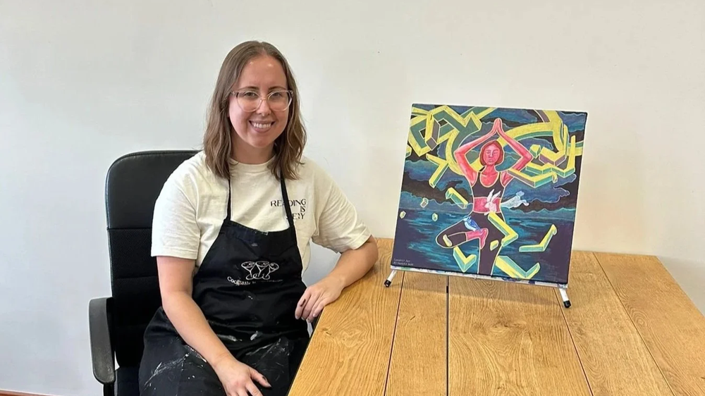Canadian artist Monica Brinkman sitting beside one of her mixed media yoga paintings