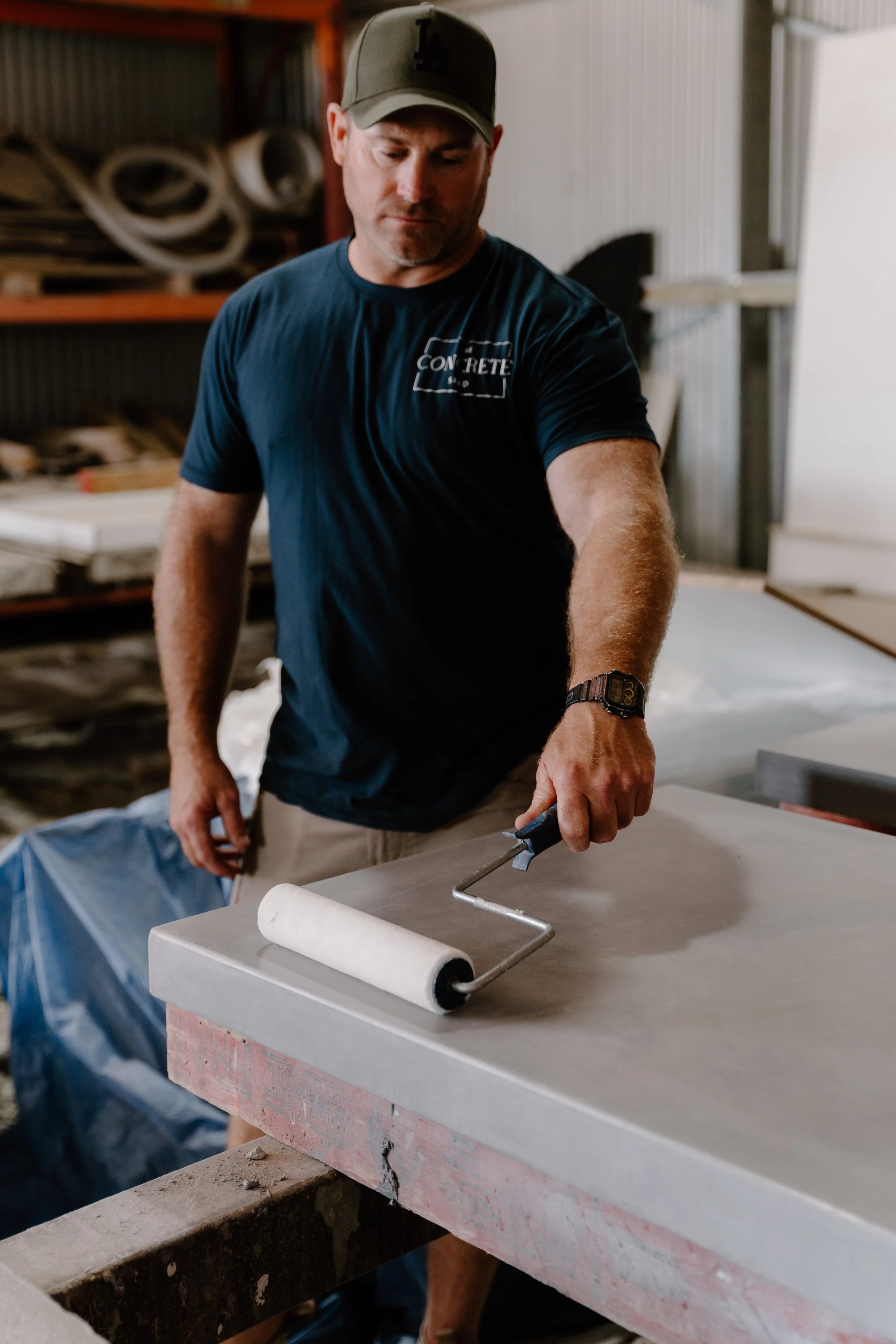 Man using a paint roller on a large flat surface in a workspace or workshop.