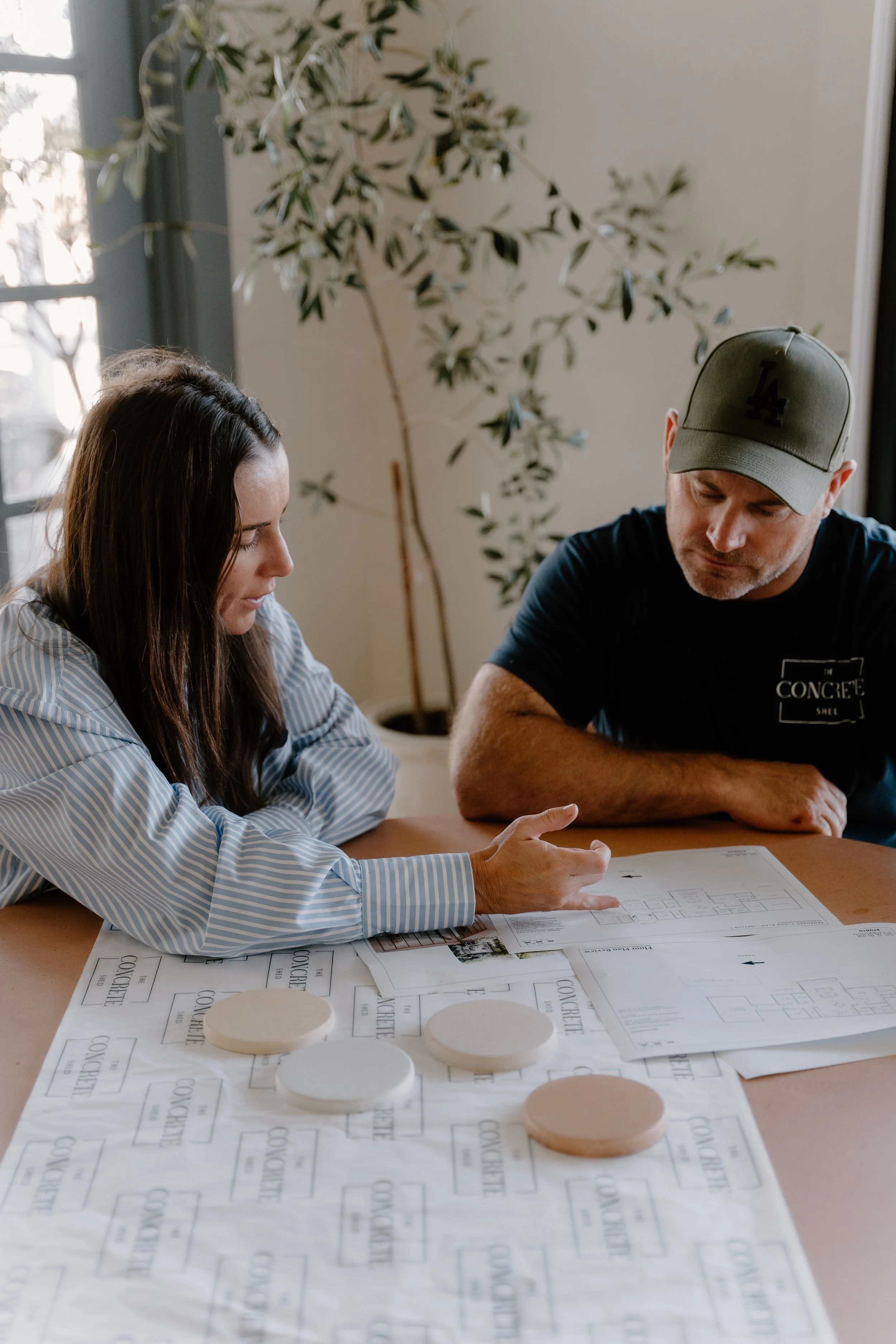 Two people reviewing architectural plans at a table with color and material samples for a construction project.