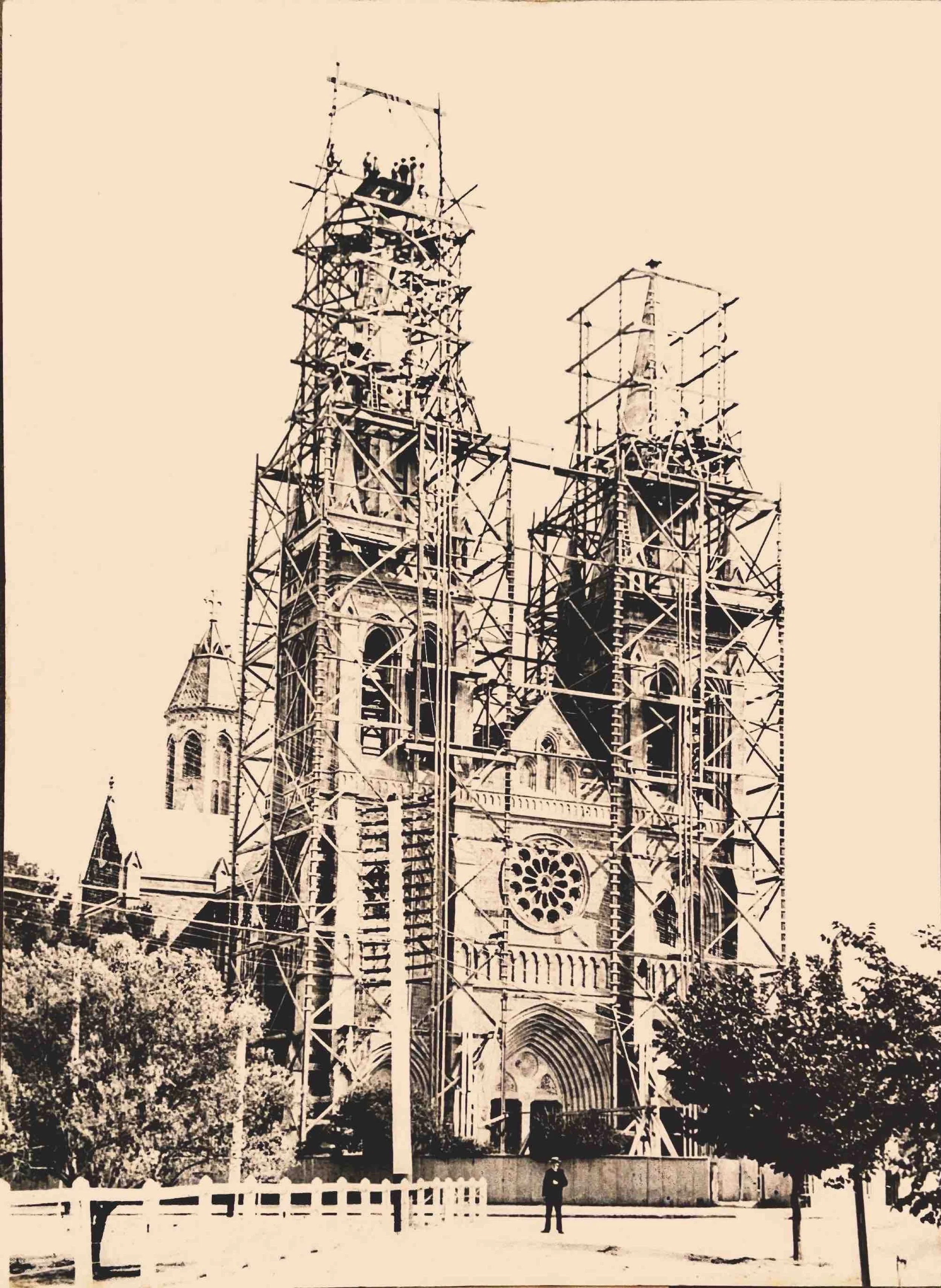 12. The Towers and Spires 1902 - The spires were completed and blessed on the 7th of December, 1902. The workmen on the platform at the top of the western tower seem to be dressed formally, perhaps for a topping ceremony. The cross is faintly visible