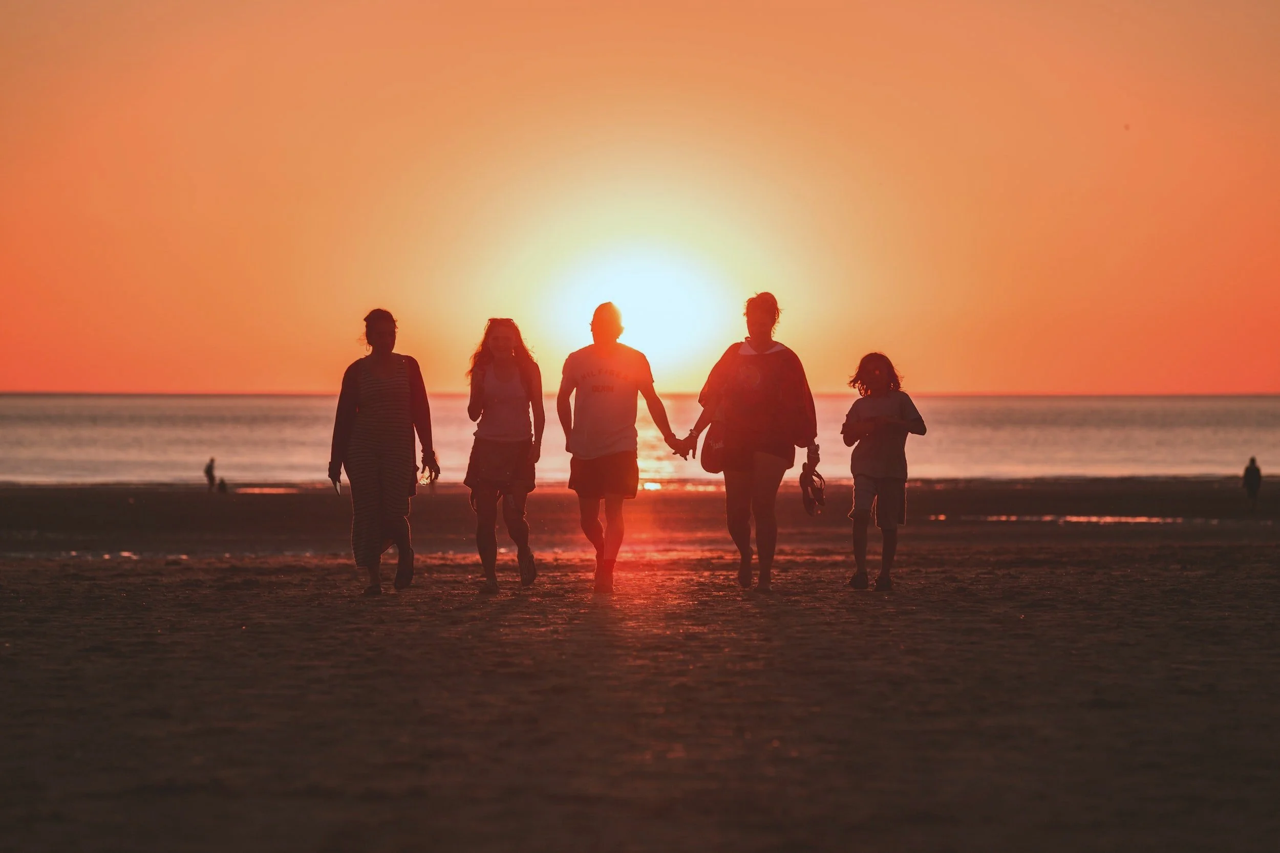 Group of people holding hands walking on beach during sunset.