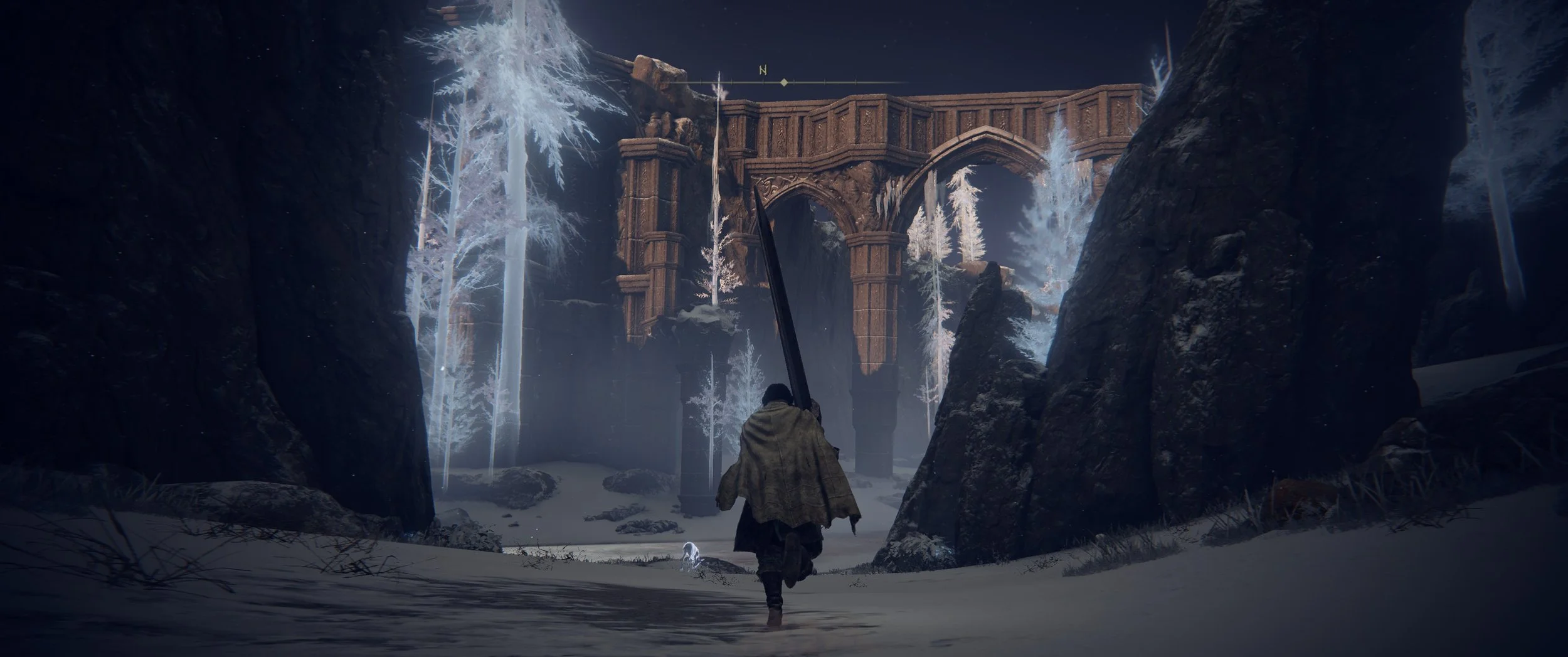 Ein wandernder Mensch mit einem großen Schwert geht durch eine verschneite Landschaft mit hohen Felsen und weißen Bäumen, im Hintergrund eine alte, verfallene Brücke.