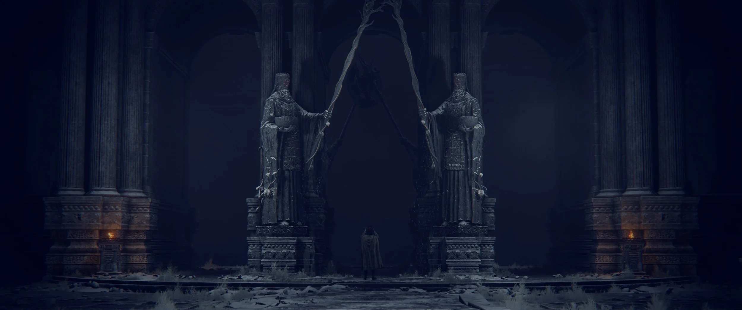 Eine große, dunkle Halle mit zwei riesigen schwarzen Statuen von Rittern, die speere halten. Im Hintergrund steht eine einzelne Person in dunkler Kleidung zwischen den Statuen. Der Boden und die Säulen sind mit Schnee bedeckt.