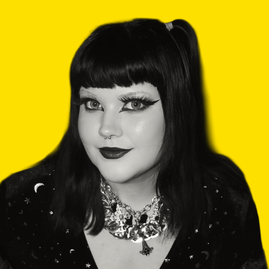 Black and white photo of a woman with dark hair and dramatic makeup, wearing a celestial-themed top and bold jewelry, with a bright yellow background.