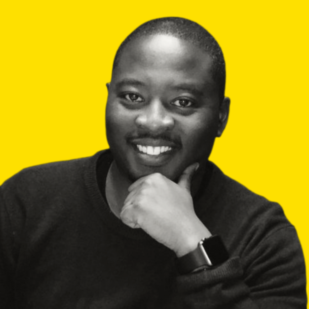 Black and white photo of a smiling man with short hair, resting his chin on his hand, wearing a dark sweater and a watch, against a bright yellow background.