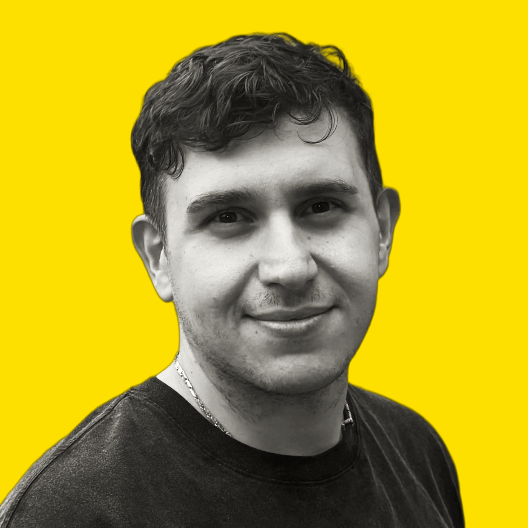 A young man with short, curly hair, smiling, in black and white, with a yellow background.