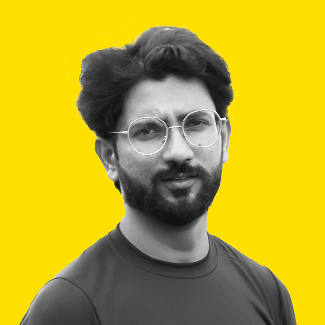 Black and white photo of a man with glasses and a beard, wearing a sports shirt, against a bright yellow background.