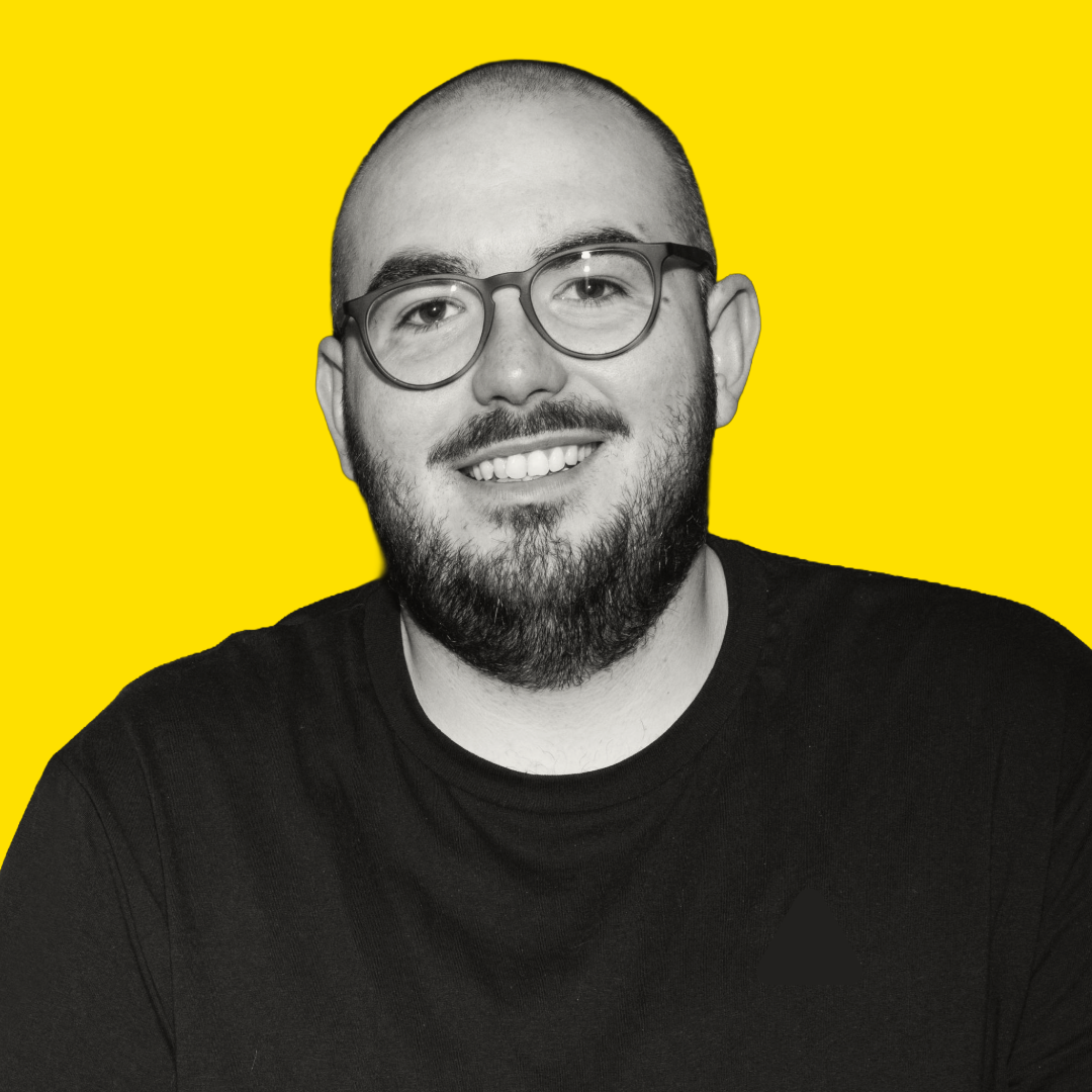 A man with glasses, a beard, and a smile, in black and white, with a yellow background.