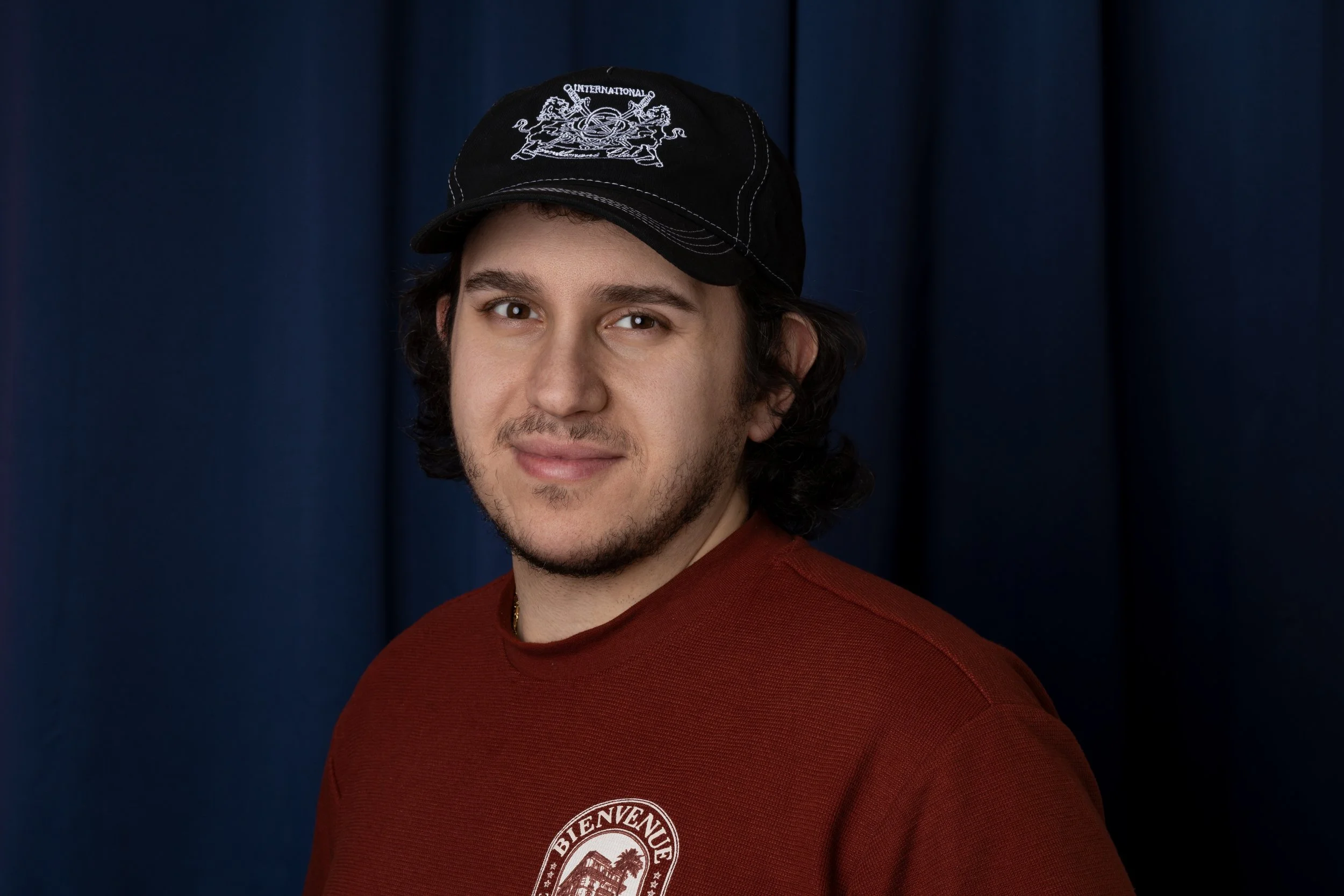 A young man with short, curly hair, smiling, in black and white, with a yellow background.