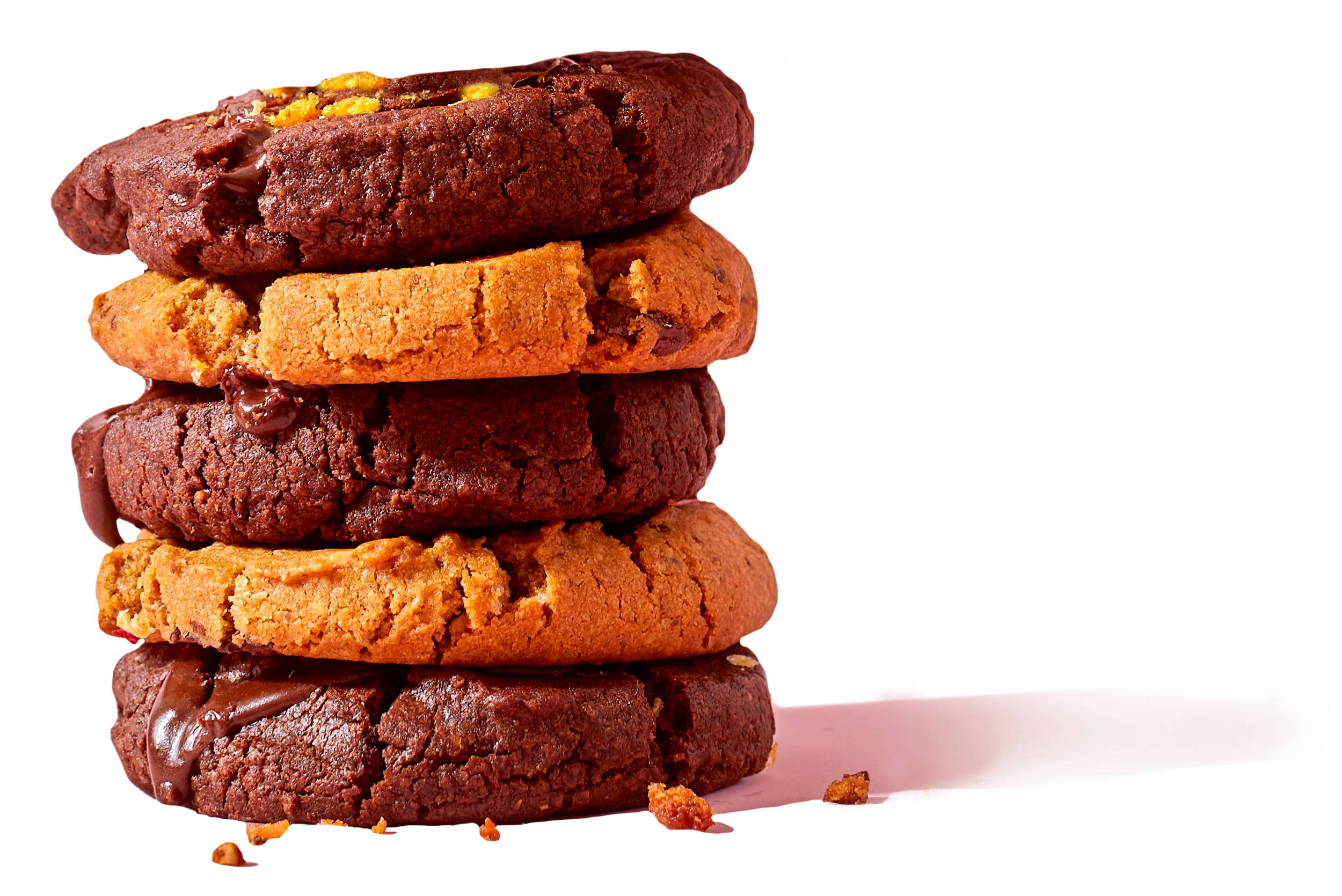 Stack of five assorted cookies, including chocolate chip, oatmeal raisin, double chocolate, peanut butter, and sugar cookies, with some crumbs around the base.