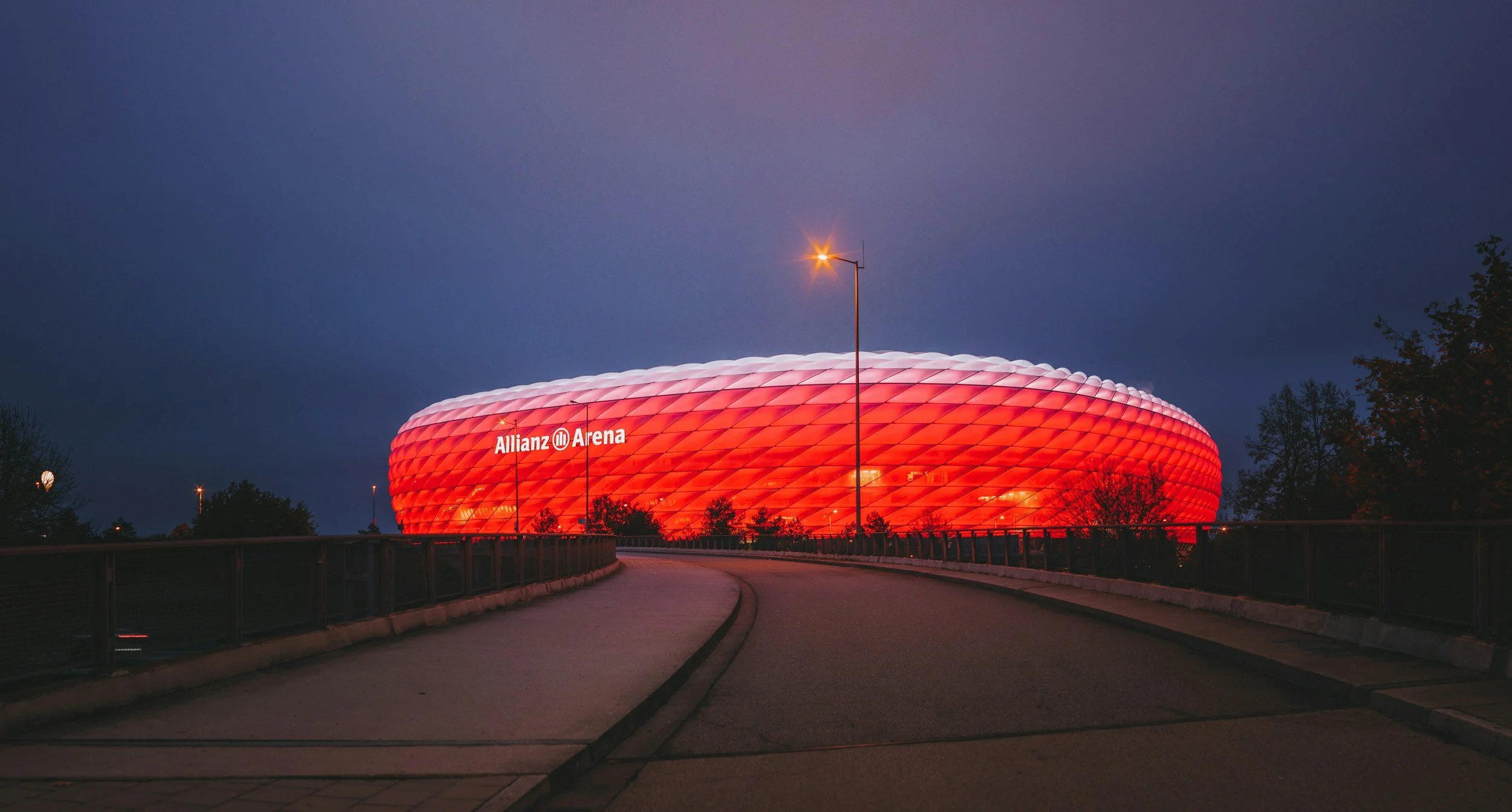 Allianz Arena, jalkapallo-otteluhalli, valoissa yöllä, sininen taivas, kadulla etualalla.