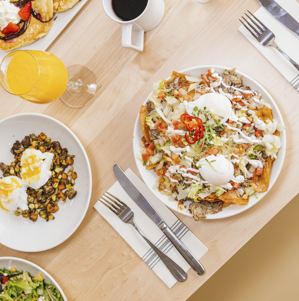 Overhead view of a breakfast table with coffee, orange juice, and plated eggs and sides