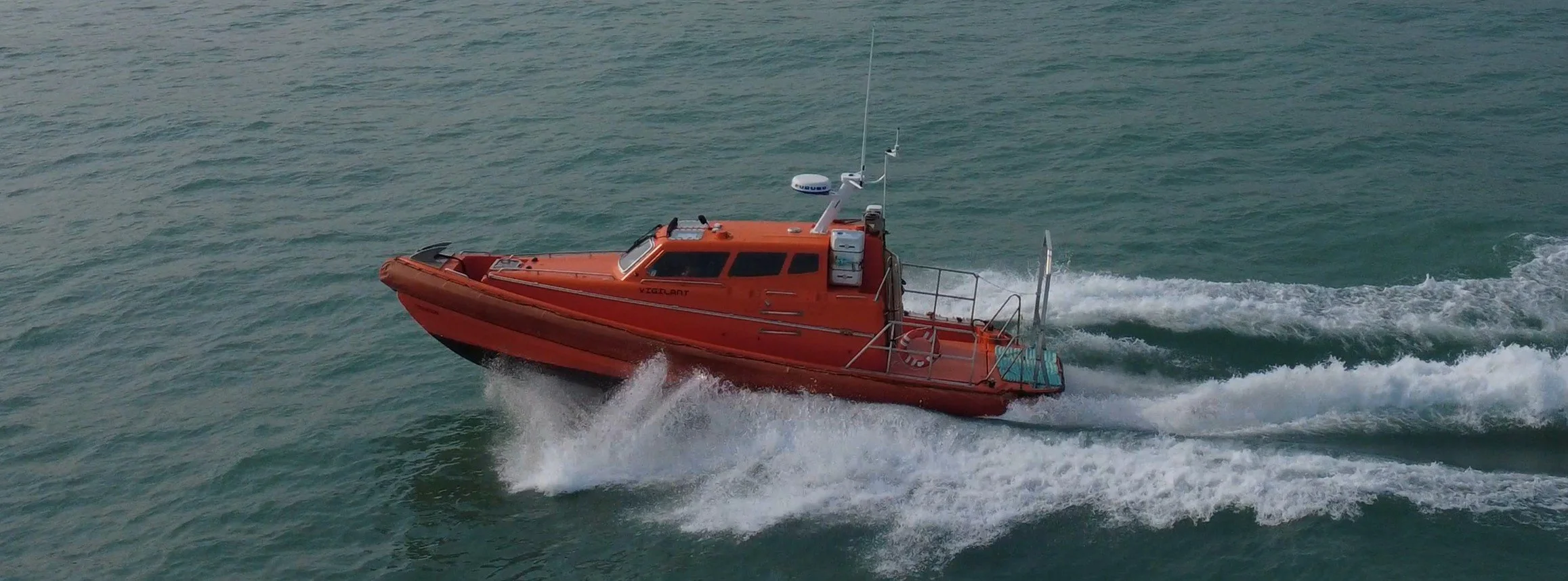 A bright orange rescue boat speeding across the water, creating white waves behind it.