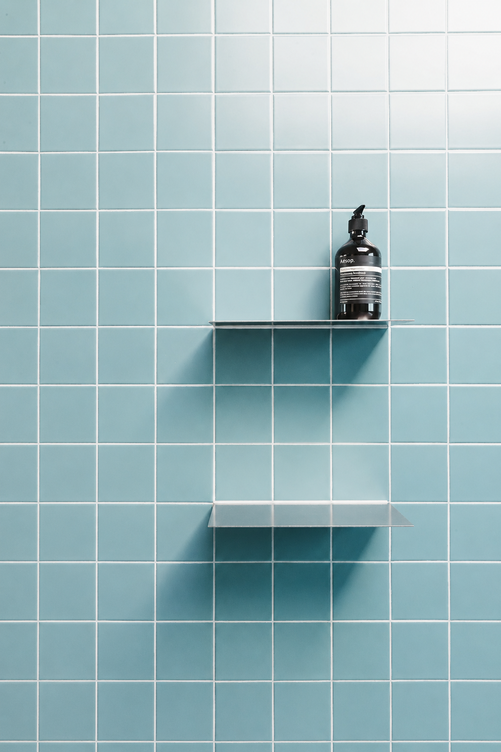 Een zwarte fles op een metalen plankje aan een blauwe betegelde muur in de douche.