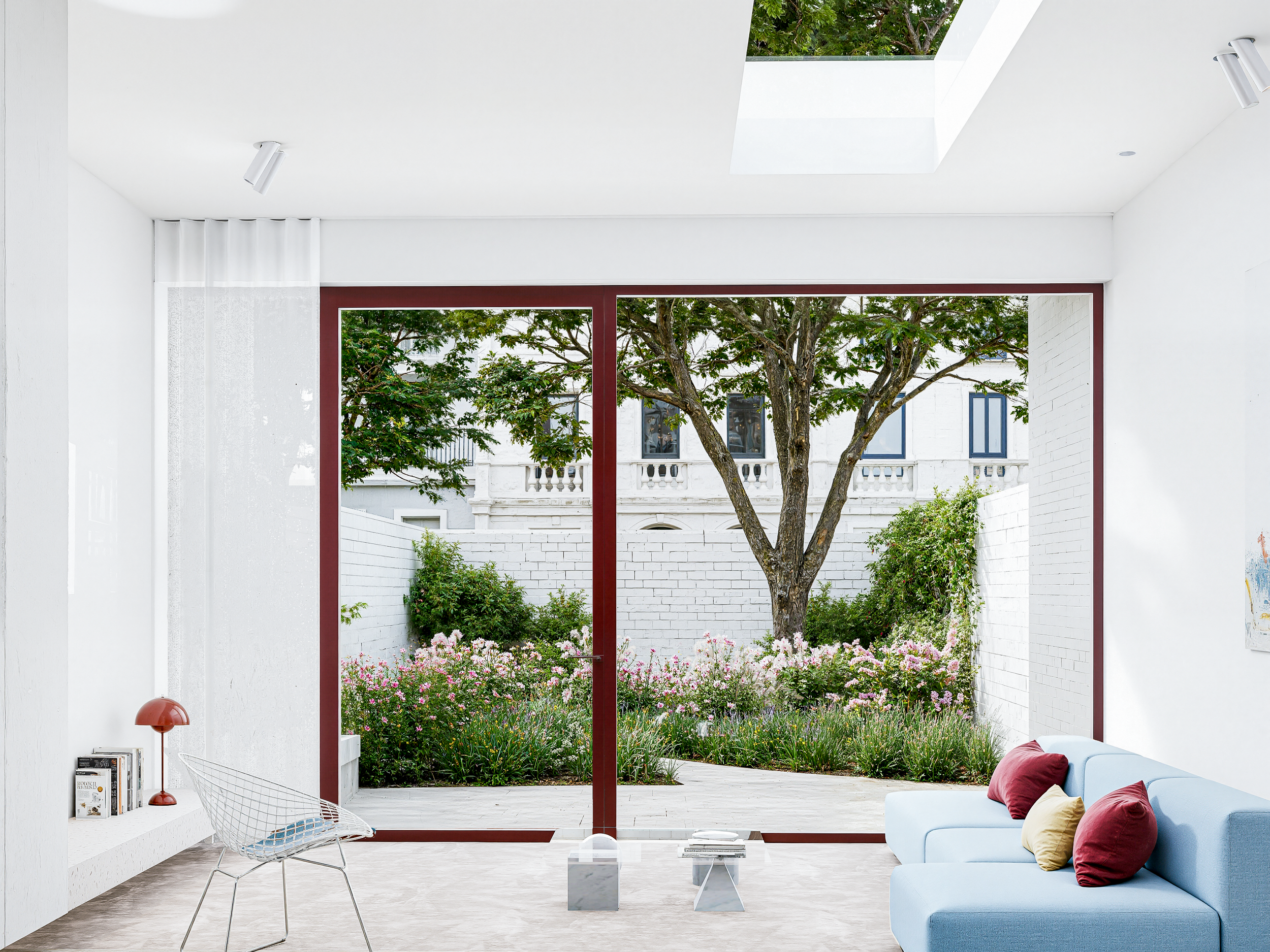 Interieur van een modern huis met grote glasdeur die uitkomt op een tuin met bomen en bloemen.