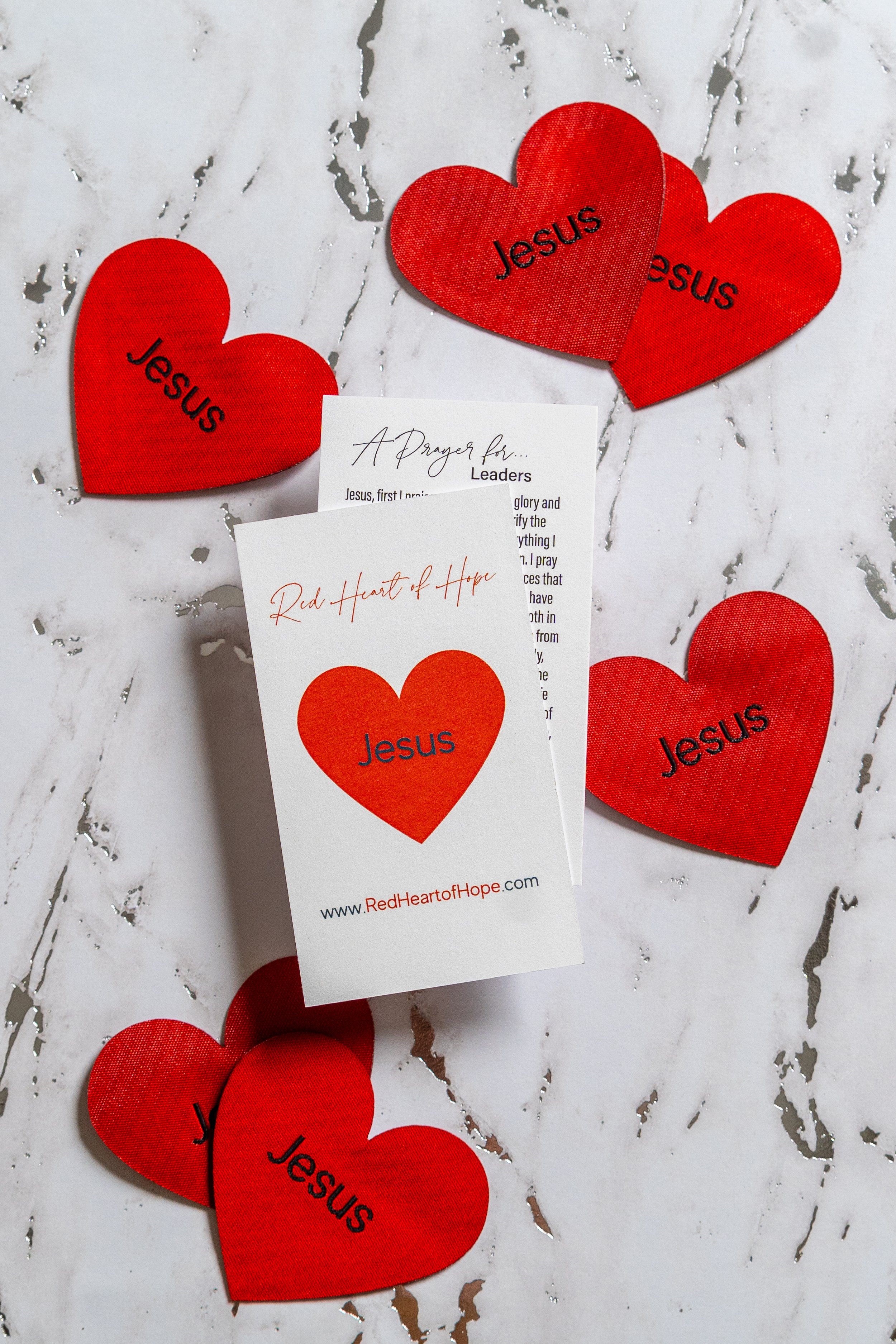 Red felt hearts with the word "Jesus" printed on each, along with a card that says "A Prayer for Leaders" and another that says "Red Heart of Hope" with a website URL.