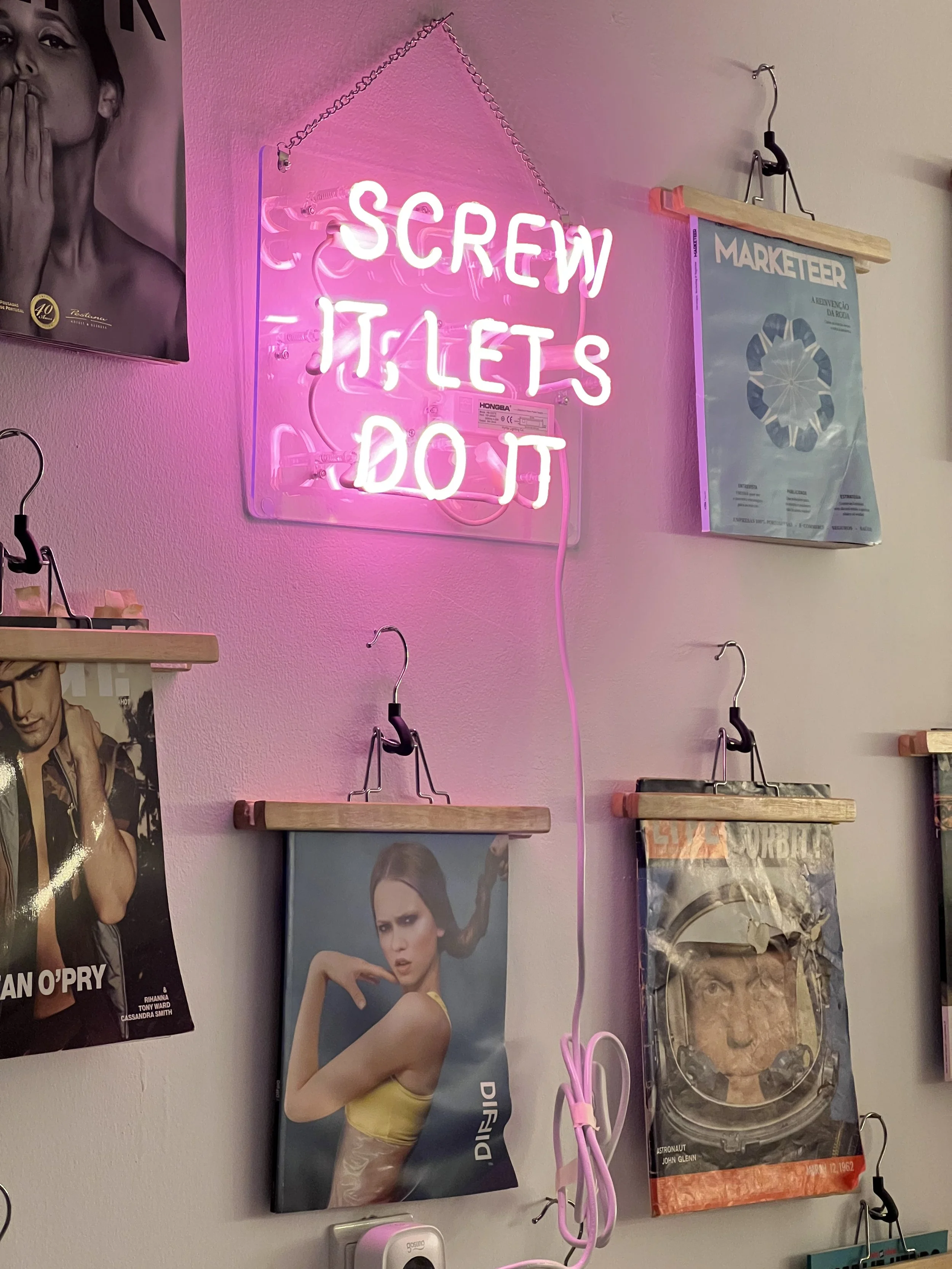 A pink neon sign on a wall that says, 'SCREW IT LET'S DO IT'