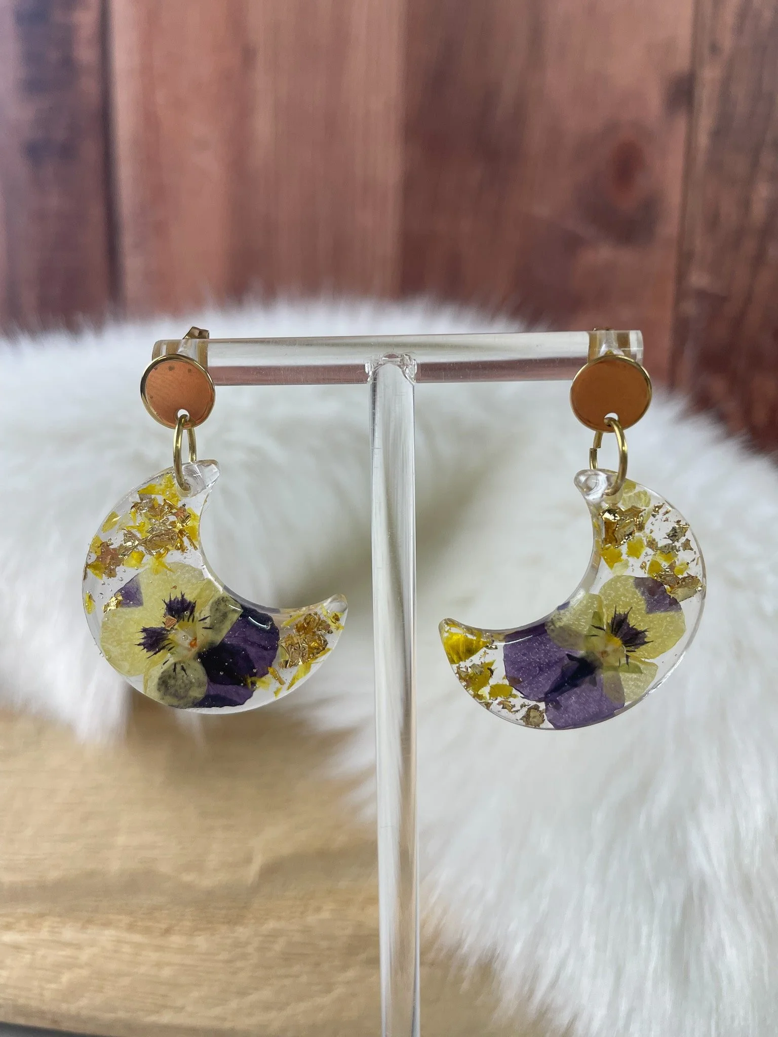 Boucles d'oreilles en résine transparente avec des fleurs séchées jaunes, violettes et or à l'intérieur, suspendues à des cercles dorés.