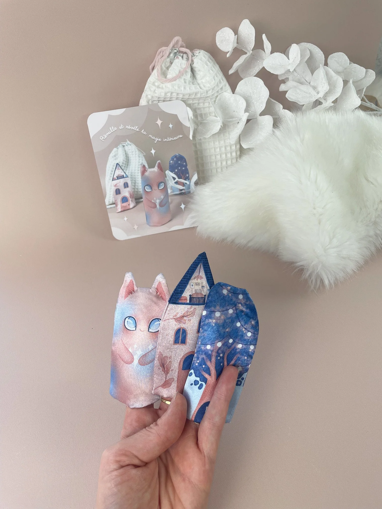 Main tenant trois marionnettes de feuilles de livres avec des dessins de petit chat et de château, et un miroir blanc dans le décor.