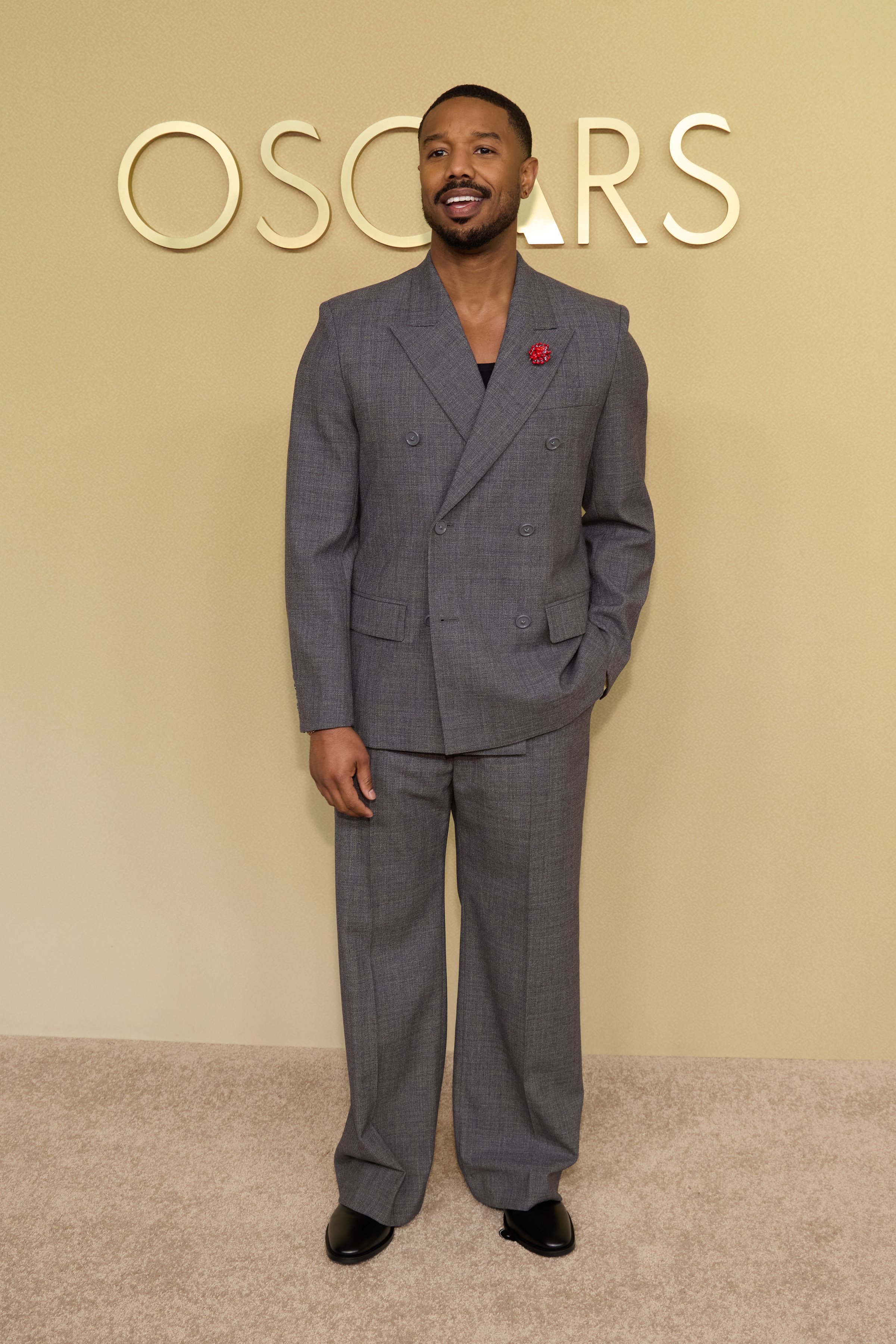 Michael B. Jordan in a charcoal grey double-breasted Balenciaga suit and gold brooch at the 98th Oscars Nominees Luncheon.