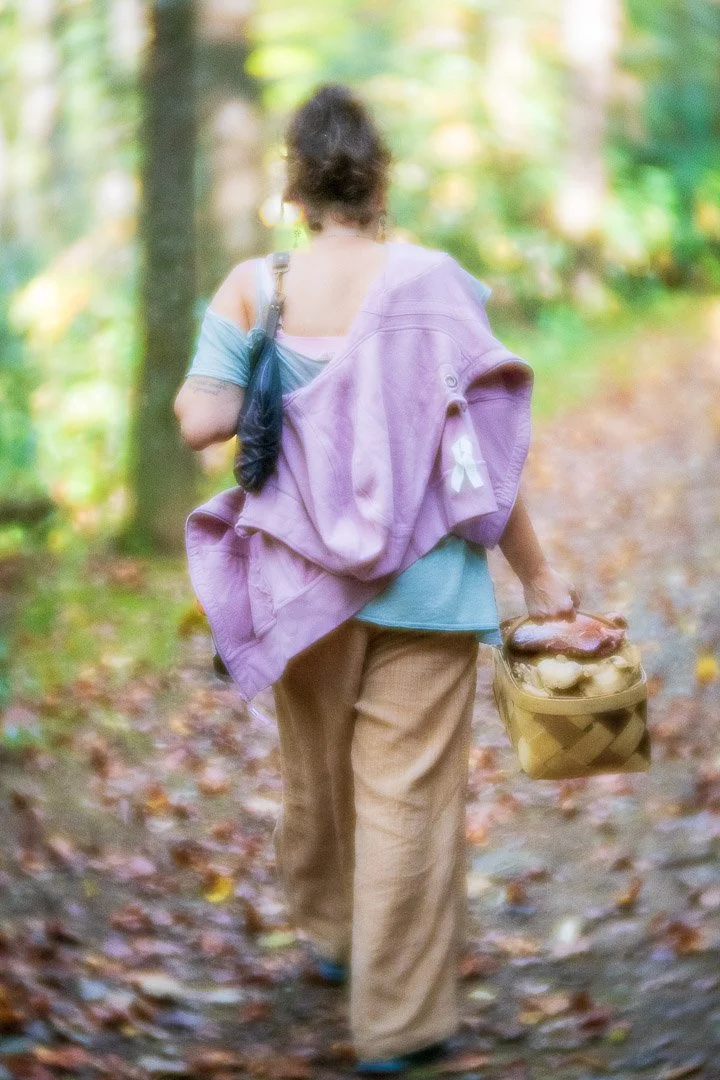 Jes walking down a forest path with a basket of foraged mushrooms.