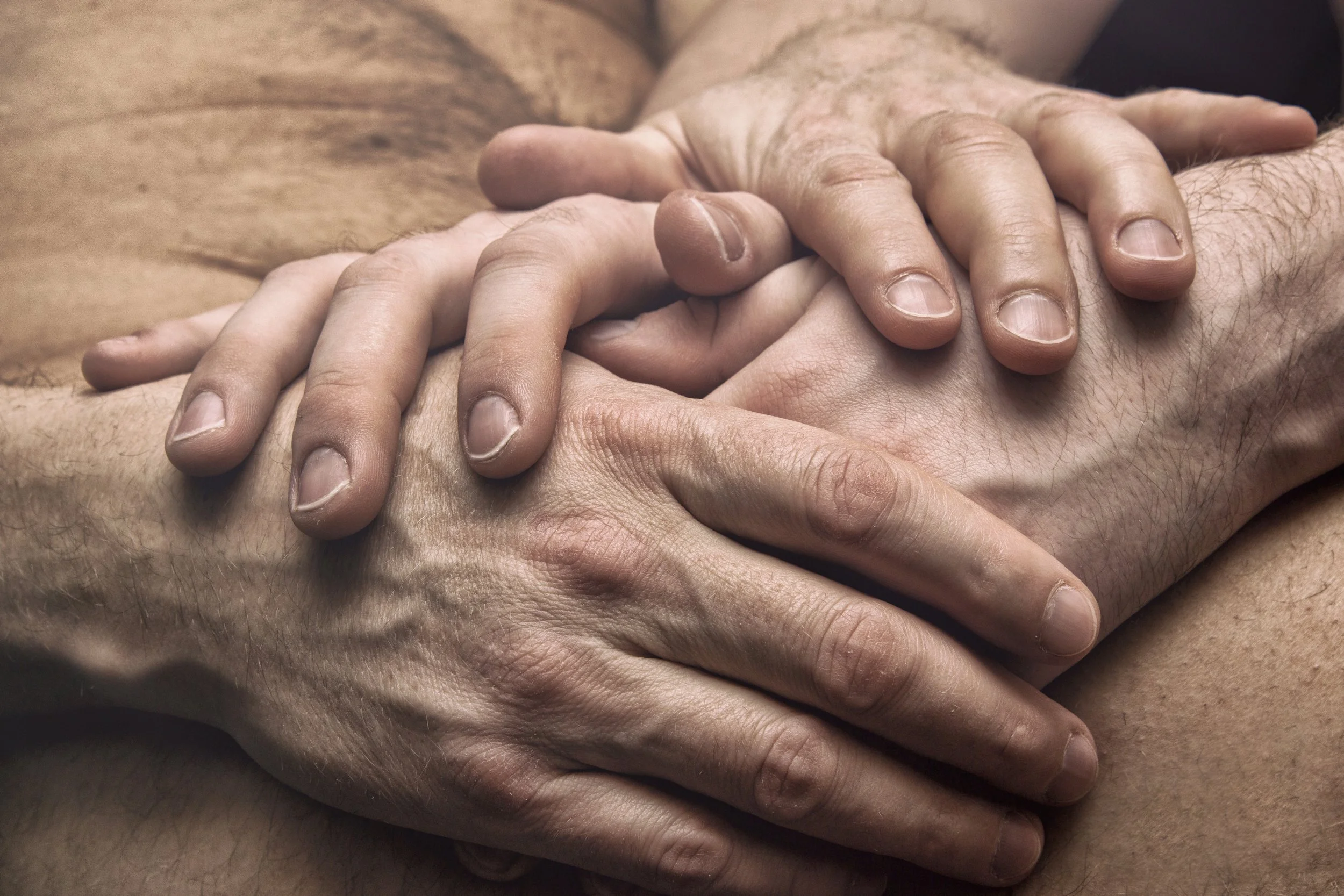 Close-up of two men’s hands gently holding each other, expressing comfort, trust, and emotional connection.