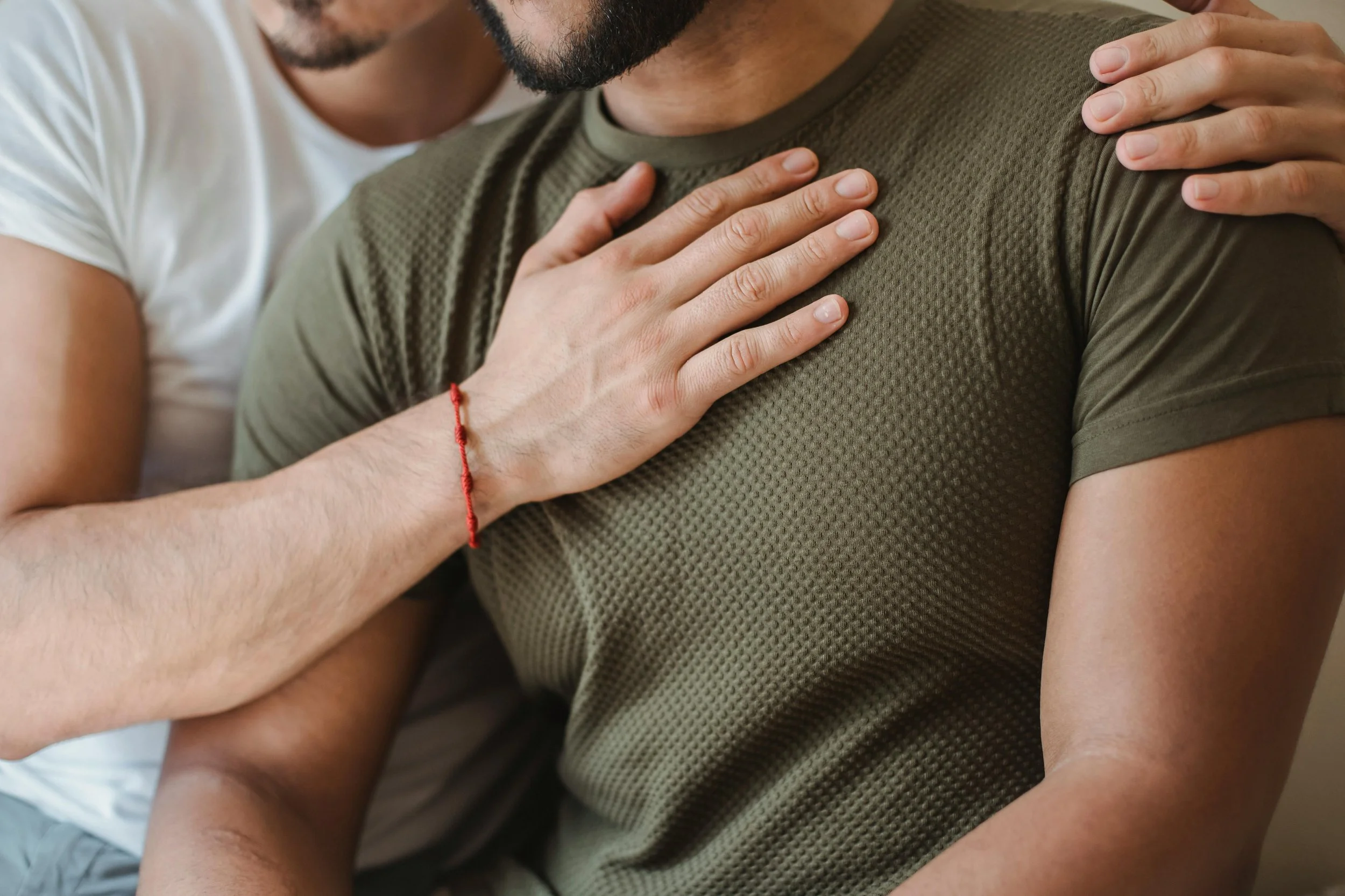 Two people, one with a beard and one wearing a white shirt, sharing an embrace with hands on each other's shoulders and chest.