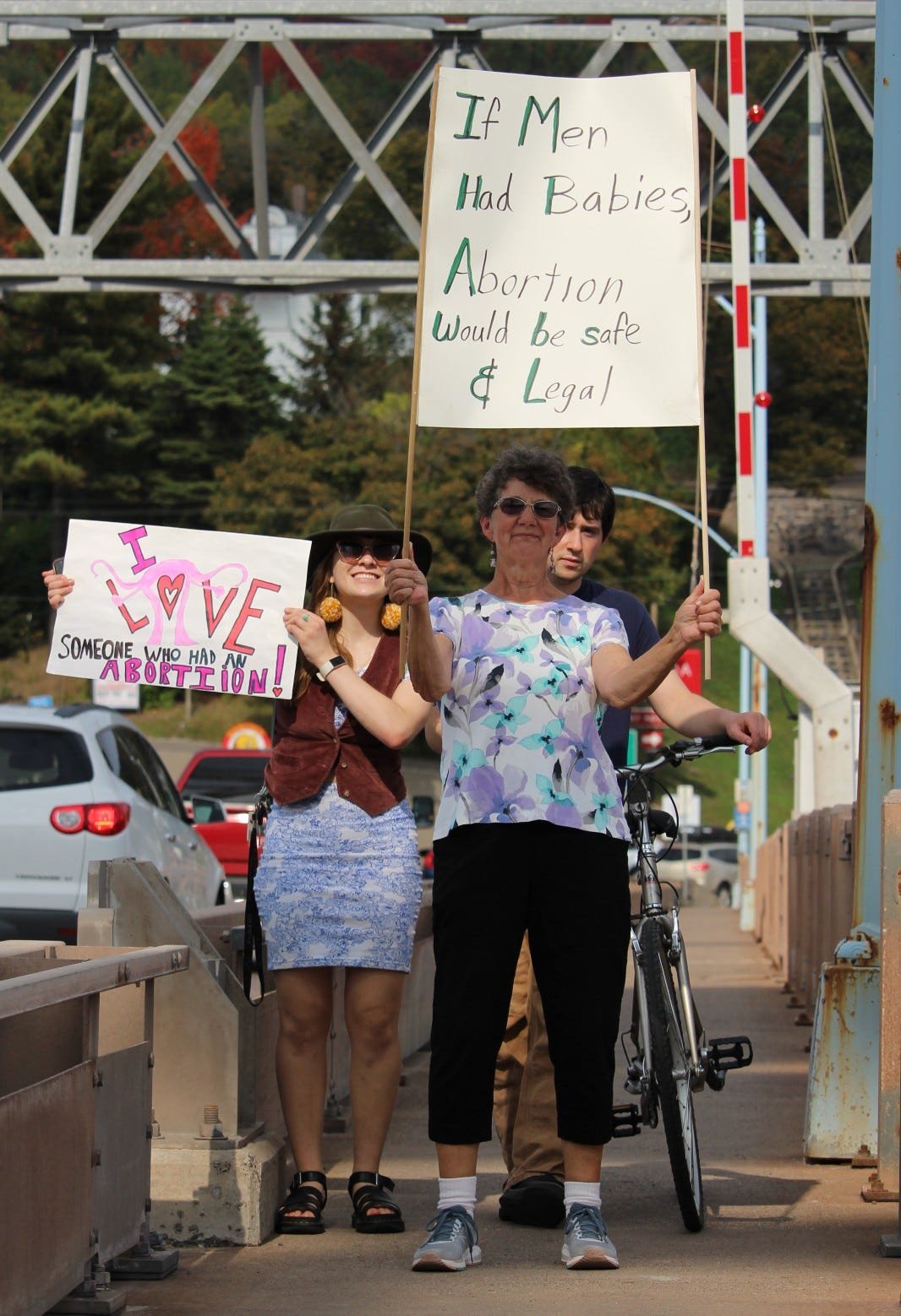  Audrey Gerard, a healthcare organizer with Michigan United (left), and Catherine Paavola, a resident of Pelkie, holding signs they carried across the bridge. 