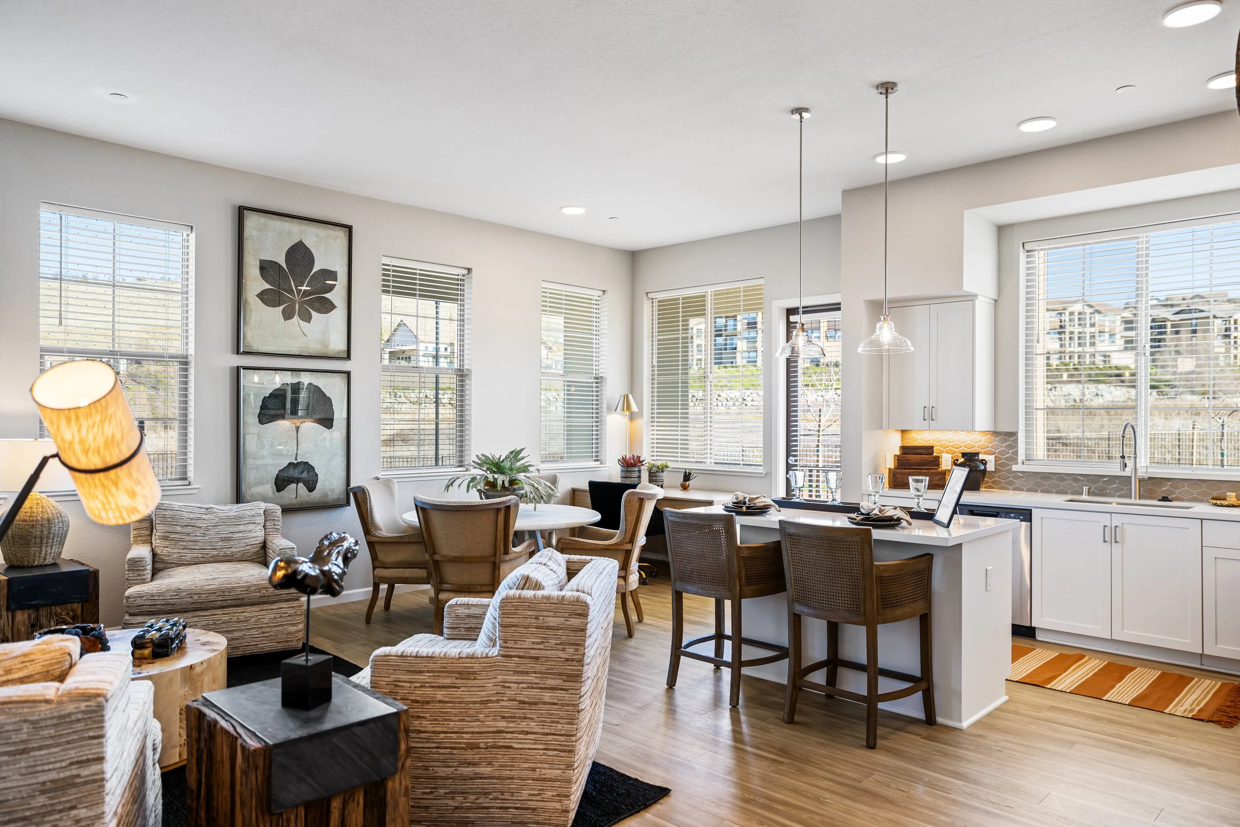 Open-concept living room and kitchen with large windows, wooden furniture, and modern decor.