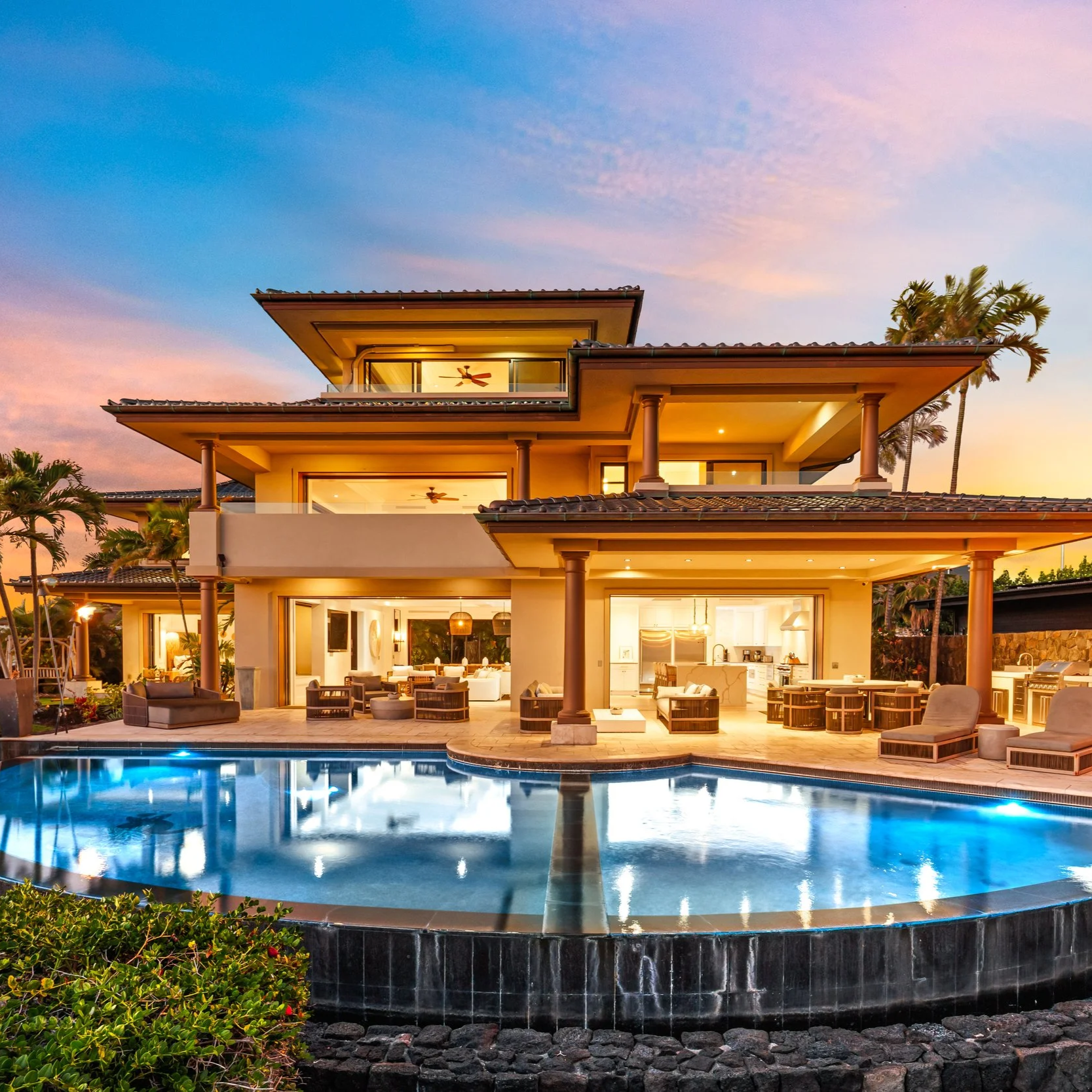 Luxury modern house with multiple levels, outdoor patio, swimming pool, and palm trees against a colorful sunset sky.