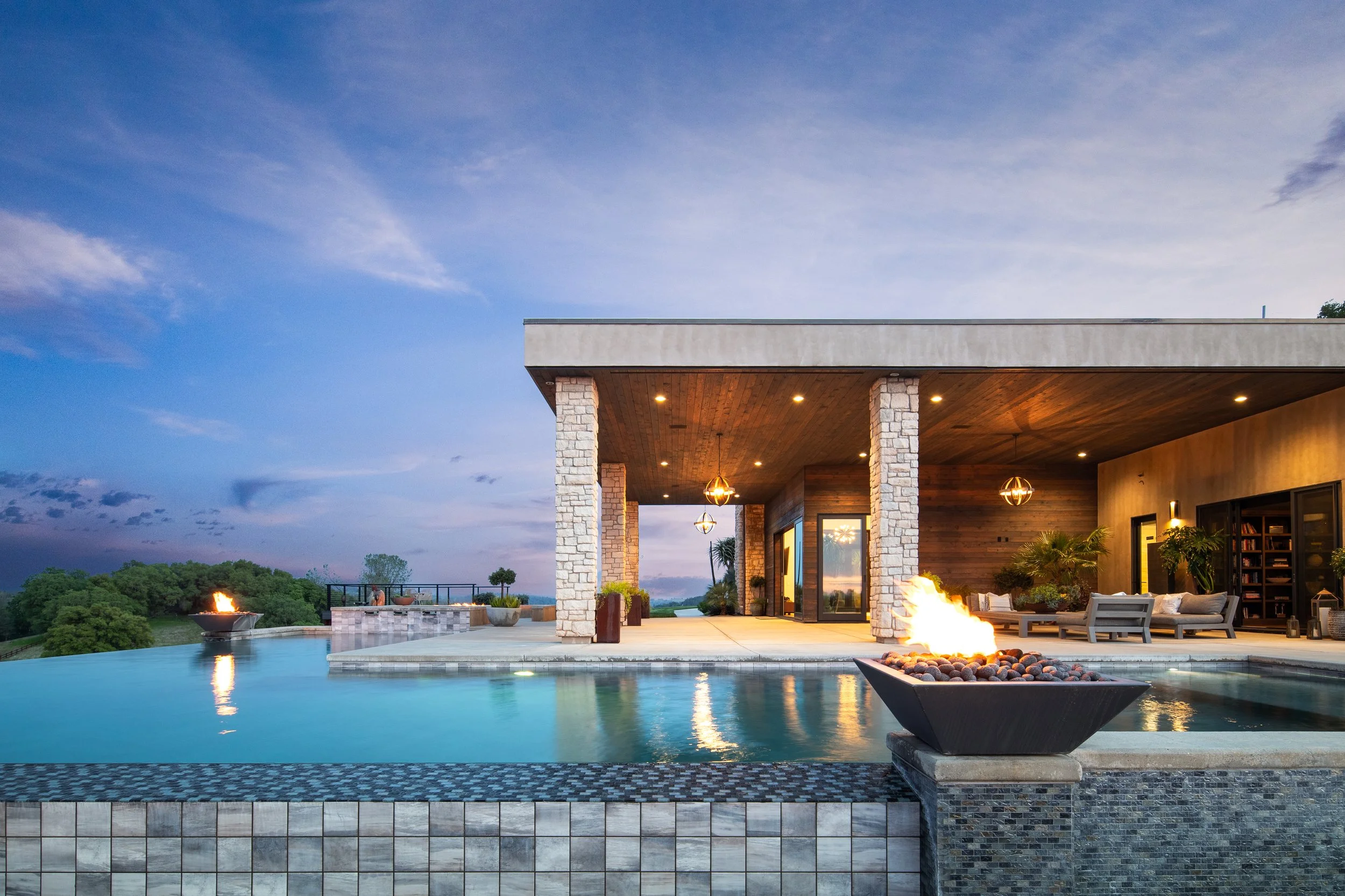 Modern house with an outdoor pool and fire features on a sunset evening.