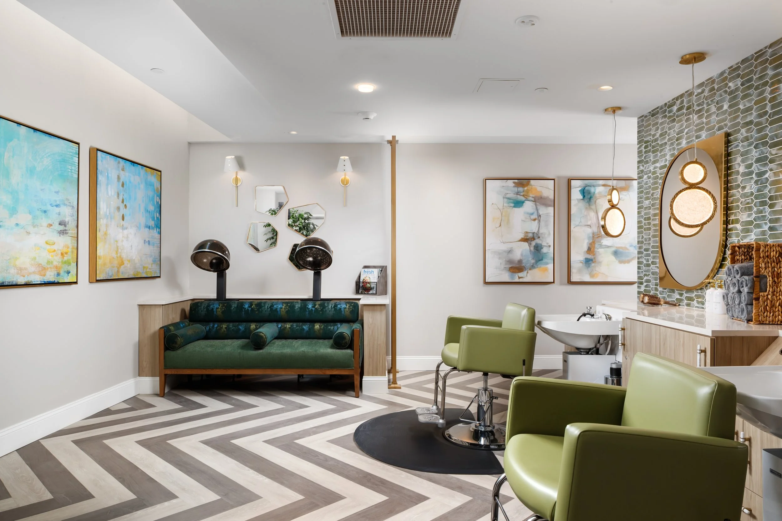 Modern salon interior with green salon chairs, hair washing station, abstract wall art, decorative mirrors, and contemporary lighting.