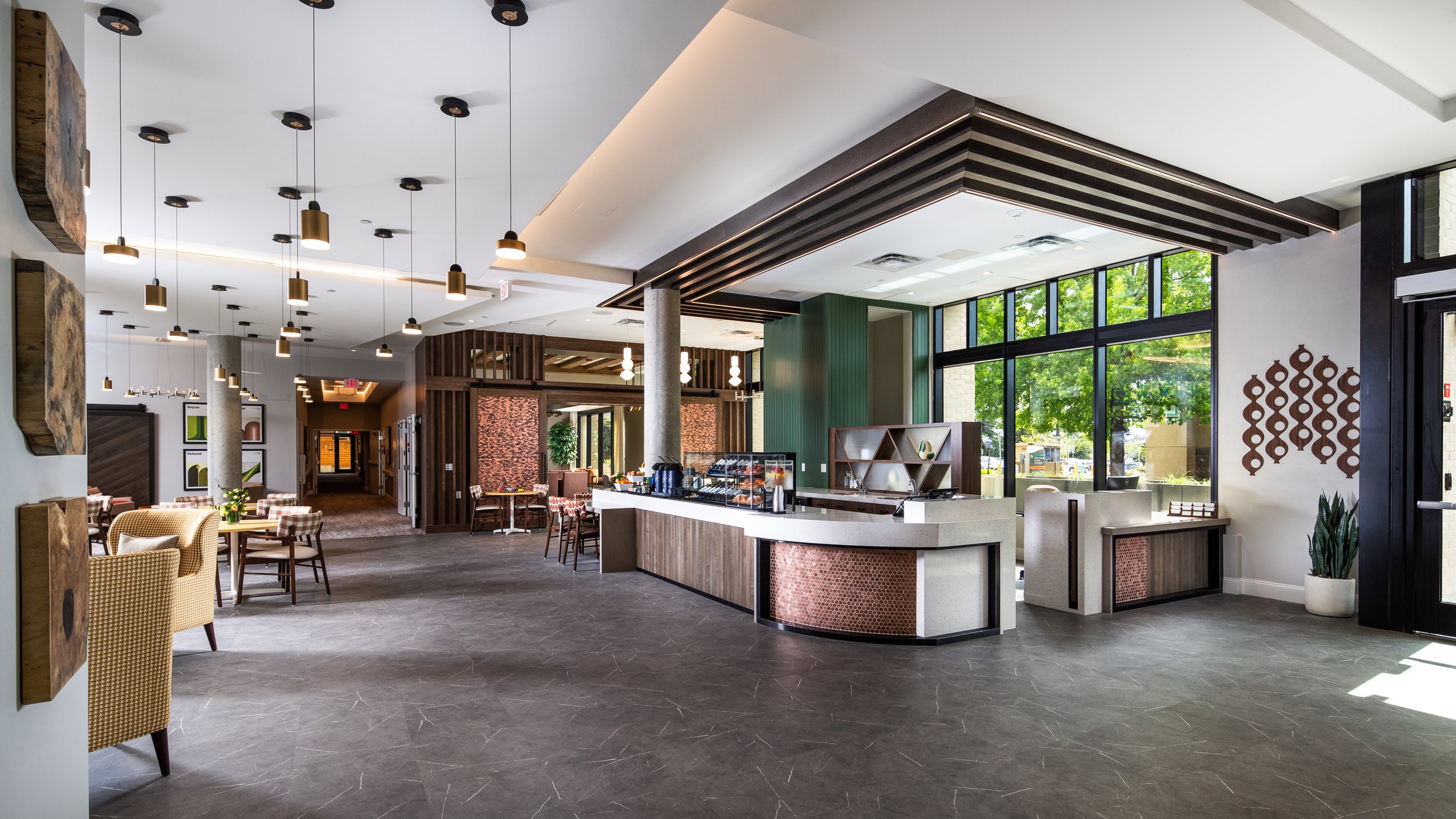 Modern restaurant interior with seating area, a coffee station, and large windows revealing greenery outside.