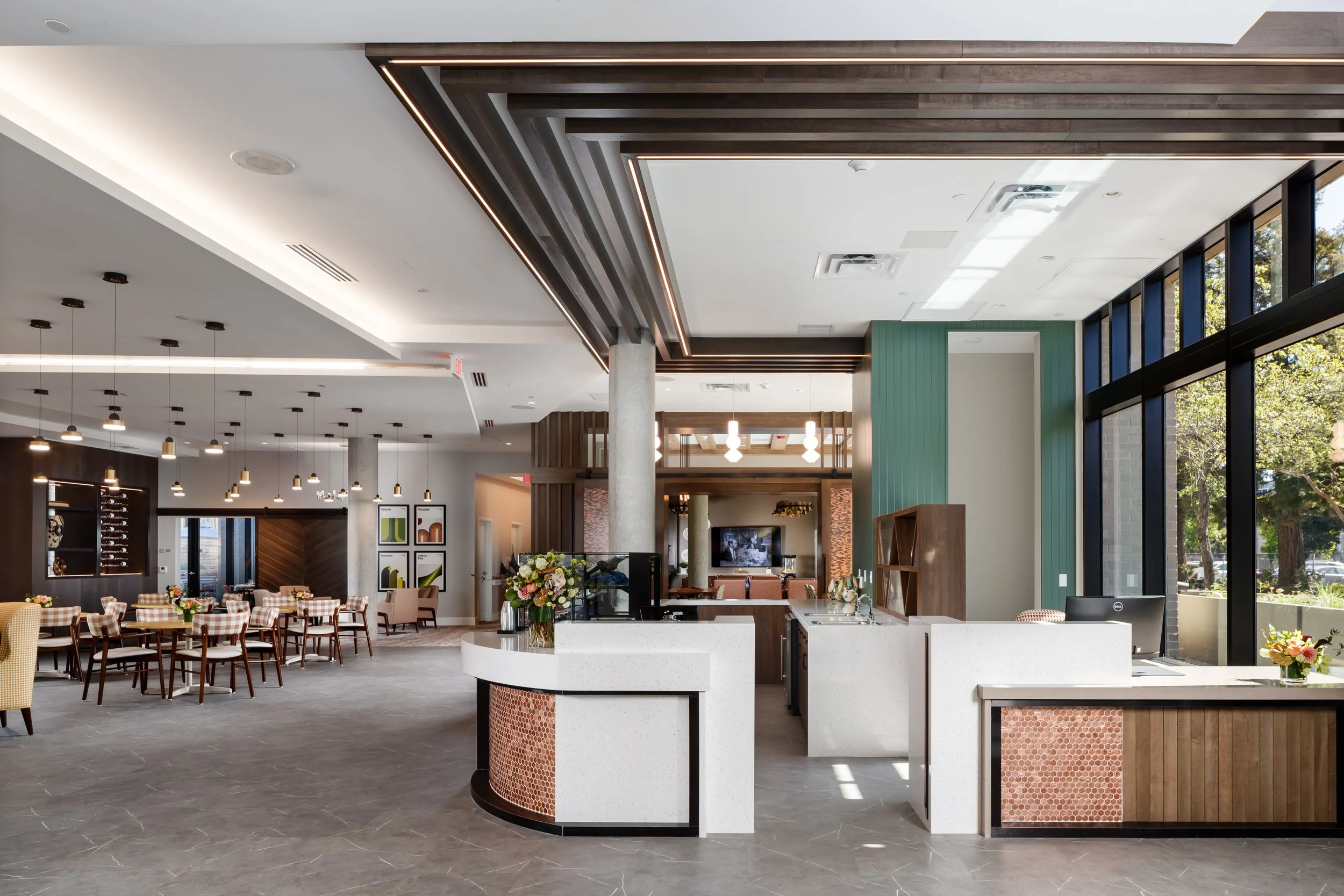 Modern restaurant interior with a white curved kitchen counter, large windows, and dining tables with checkered tablecloths.
