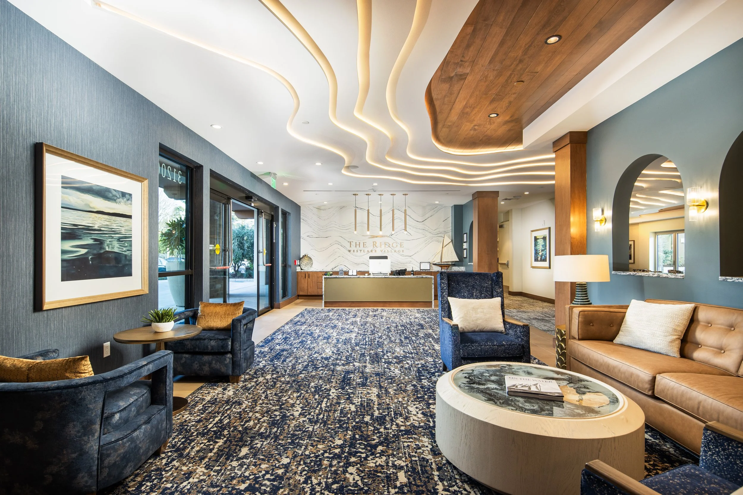 Hotel lobby with modern decor, blue and beige furniture, patterned rug, and a reception desk in the background.