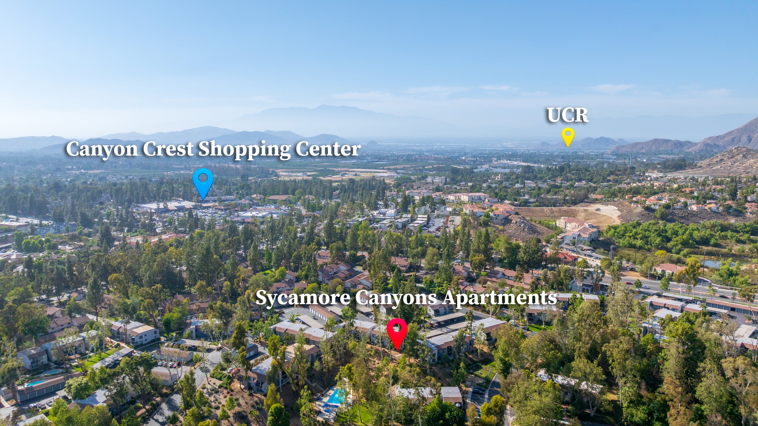 Aerial view of a suburban area showing neighborhoods with houses, trees, and roads, with mountain ranges and a cityscape in the background. The image has labels pointing to Canyon Crest Shopping Center, UCR (University of California, Riverside), and Sycamore Canyons Apartments.