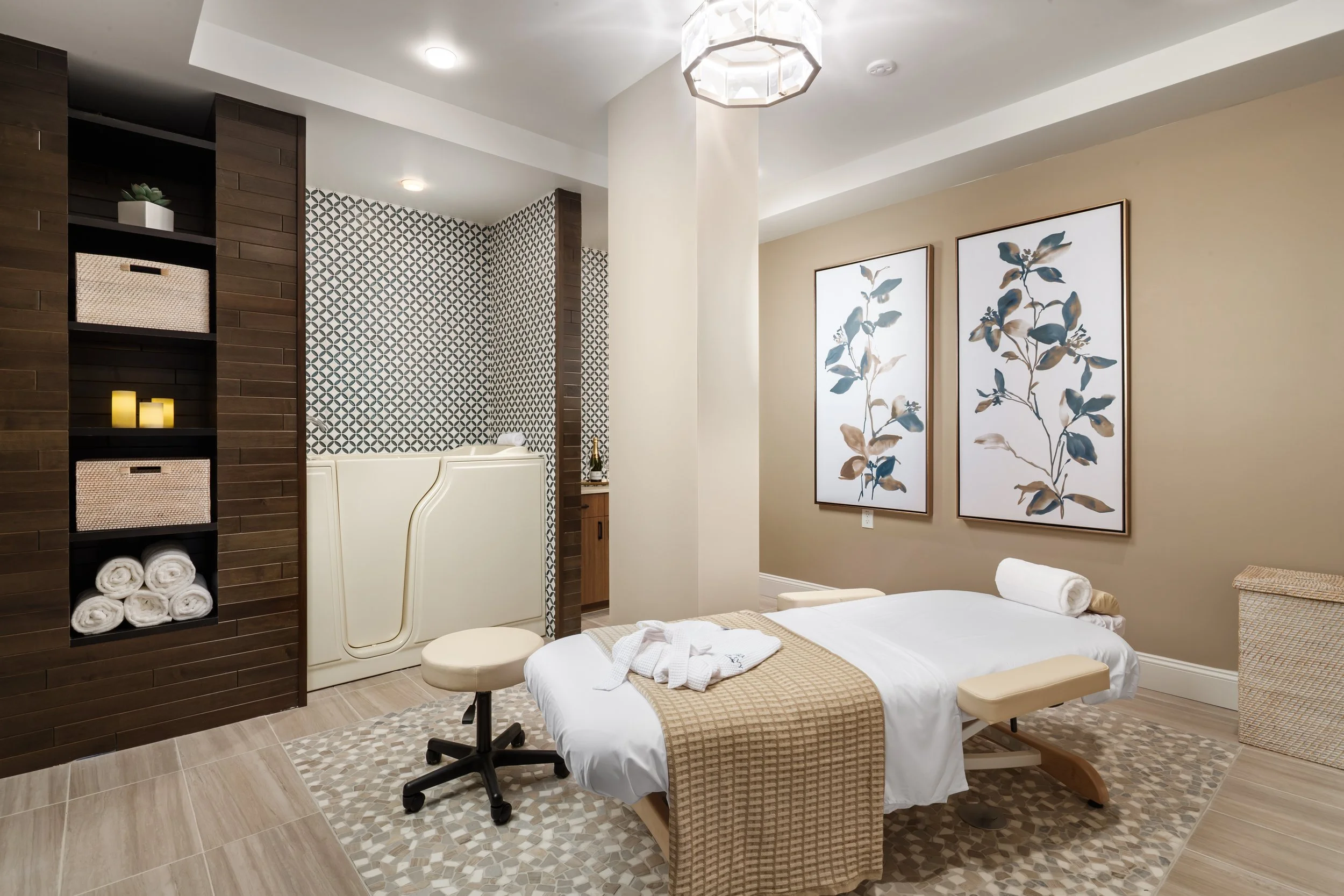 Spa room with massage bed, artwork, and shelves with candles and towels.