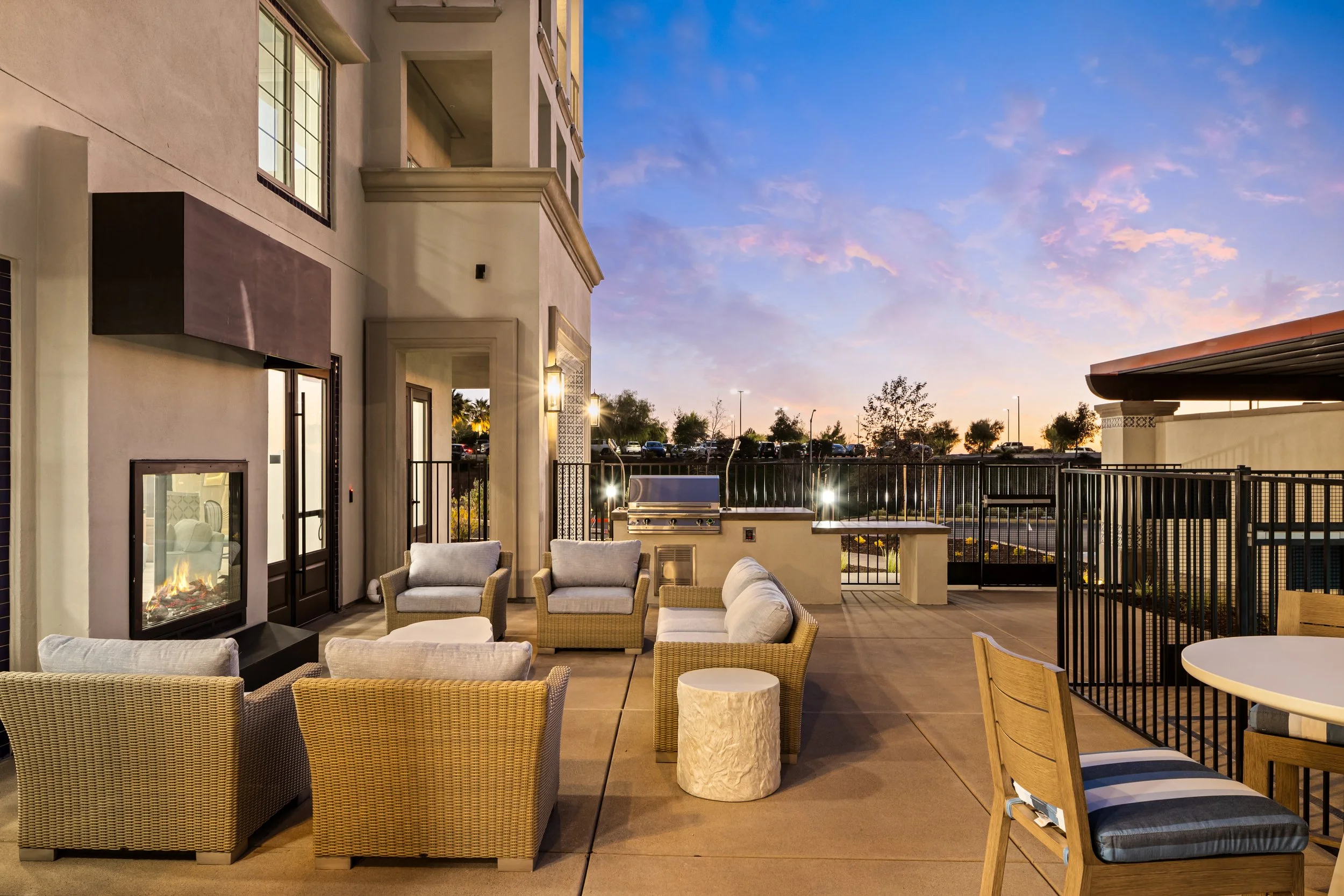 Outdoor patio with wicker chairs, a sofa, a round table, and a fireplace, with a sunset sky overhead.