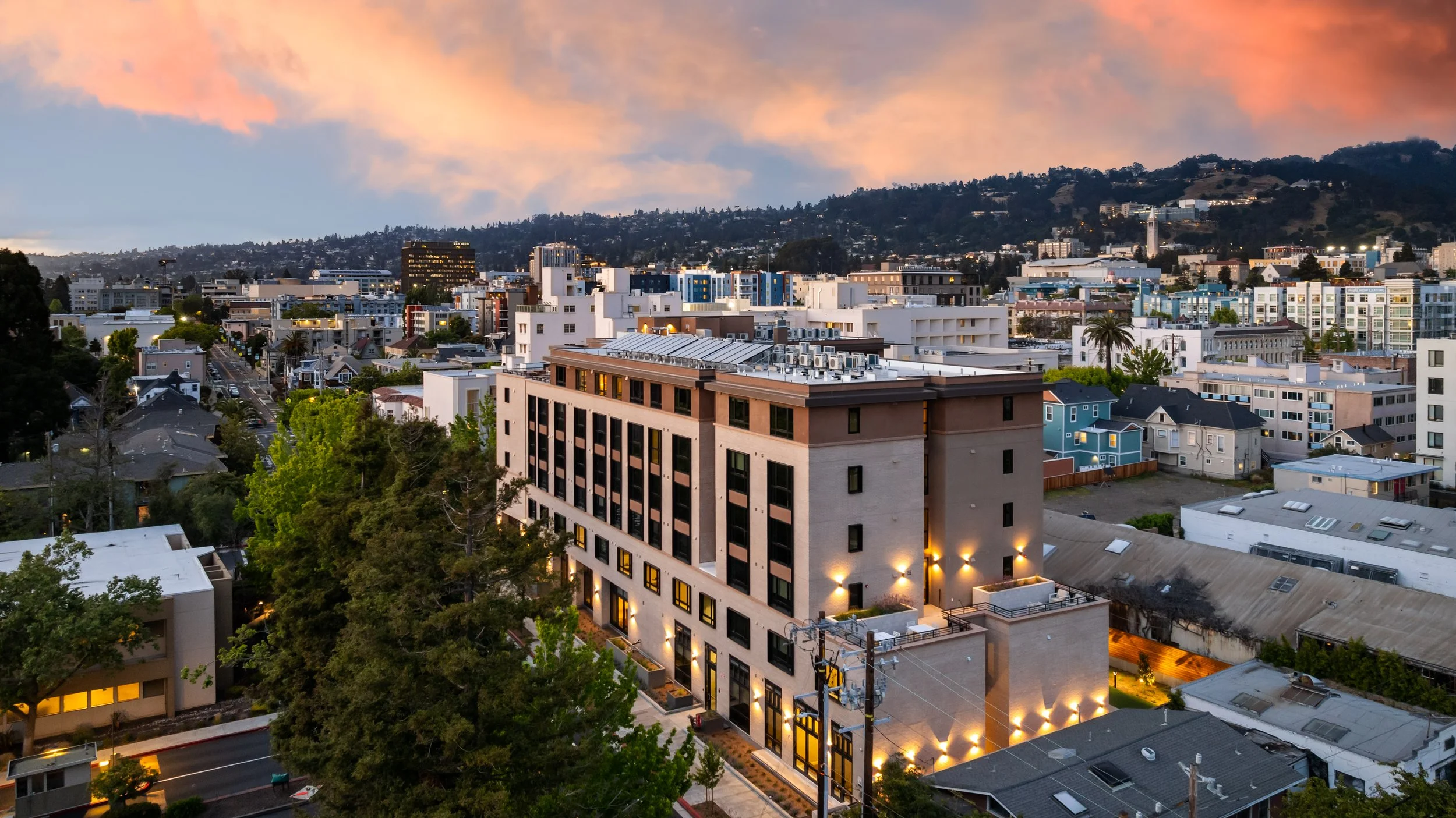Palo Alto neighborhood cityscape at sunset with tall buildings, trees, and hills in the background.