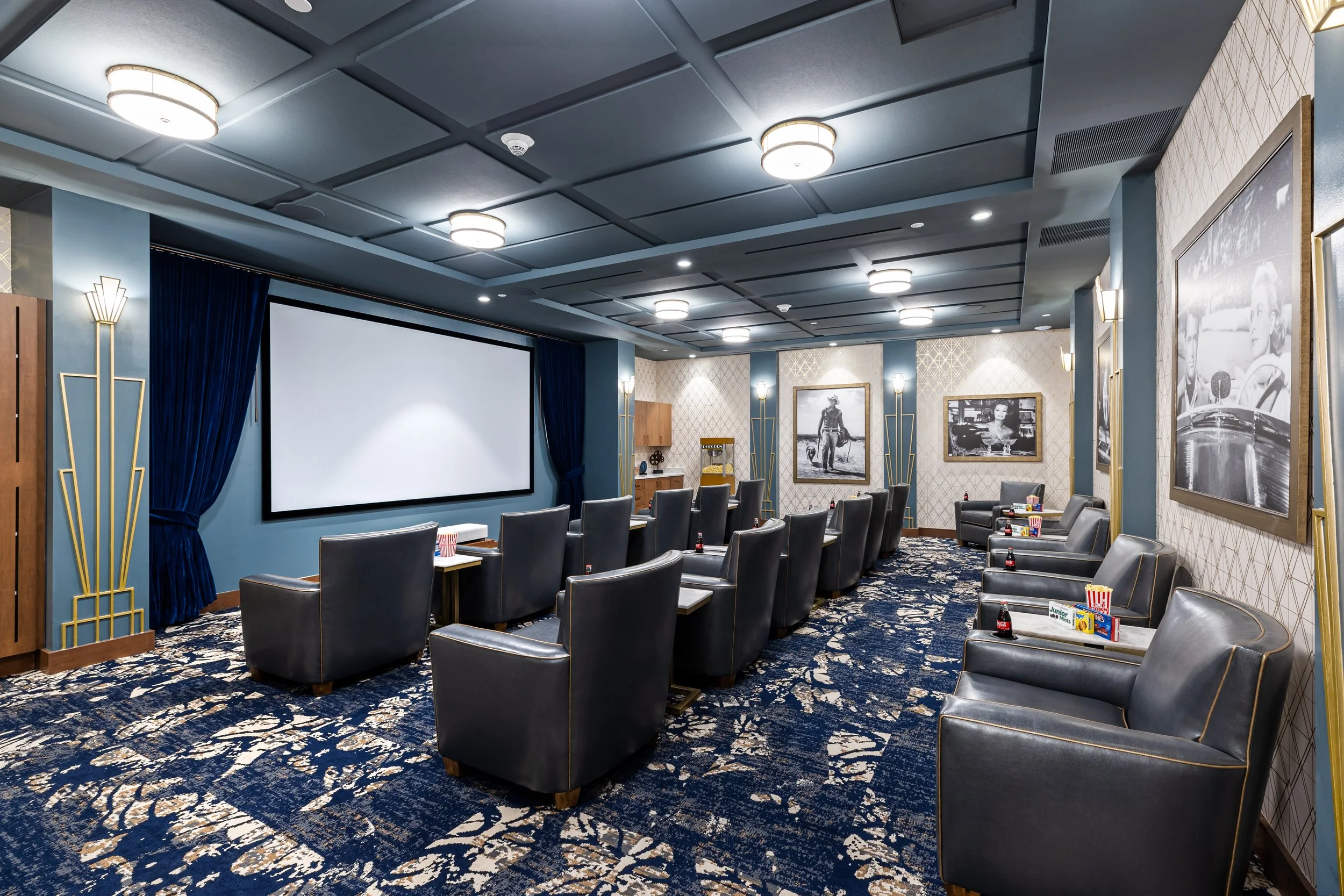 A projection room or private theater with a large screen, plush seating with armrests, and framed black-and-white photography on the walls, decorated in Art Deco style.