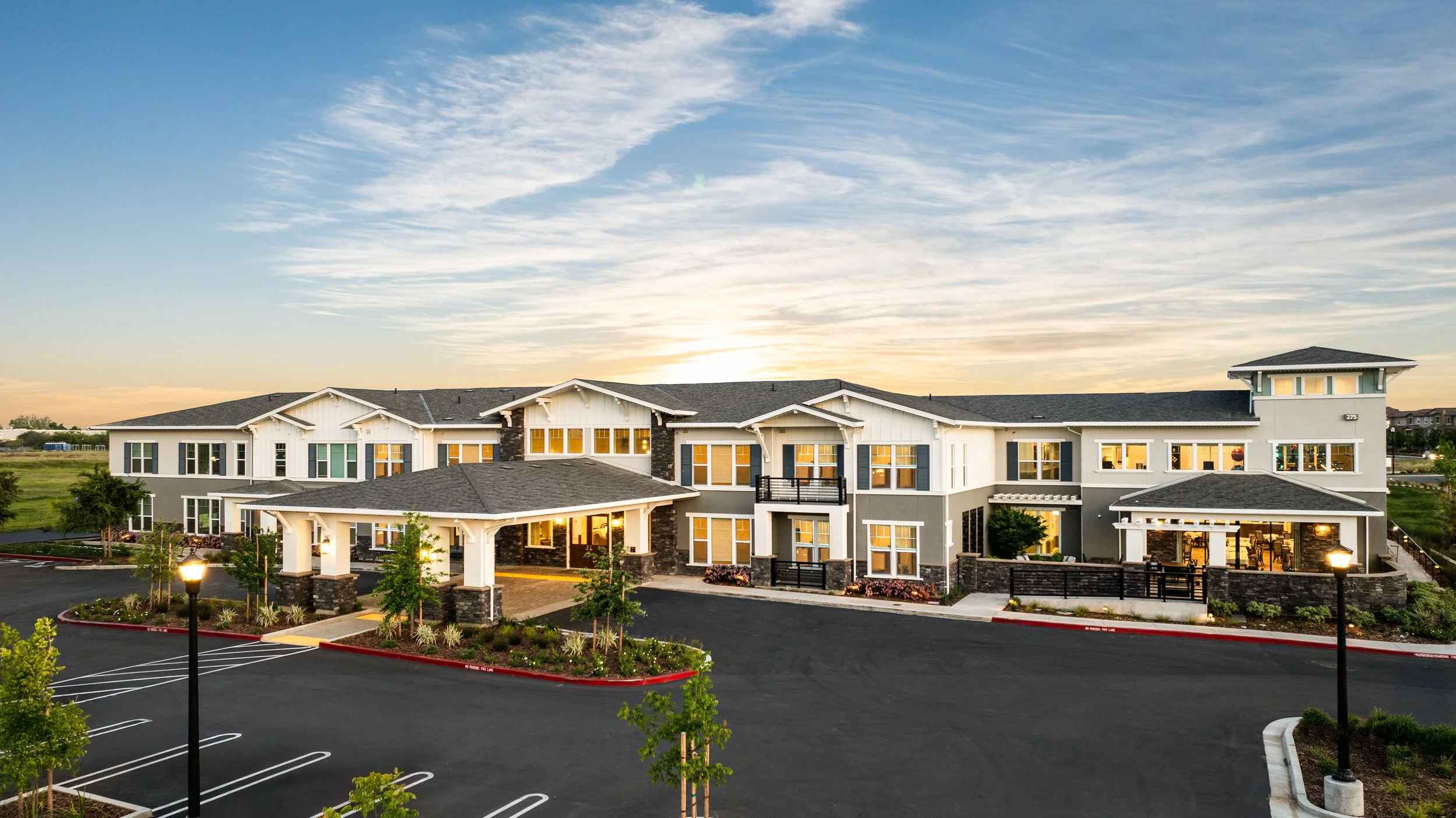 Modern apartment complex with landscaped parking lot at sunset.