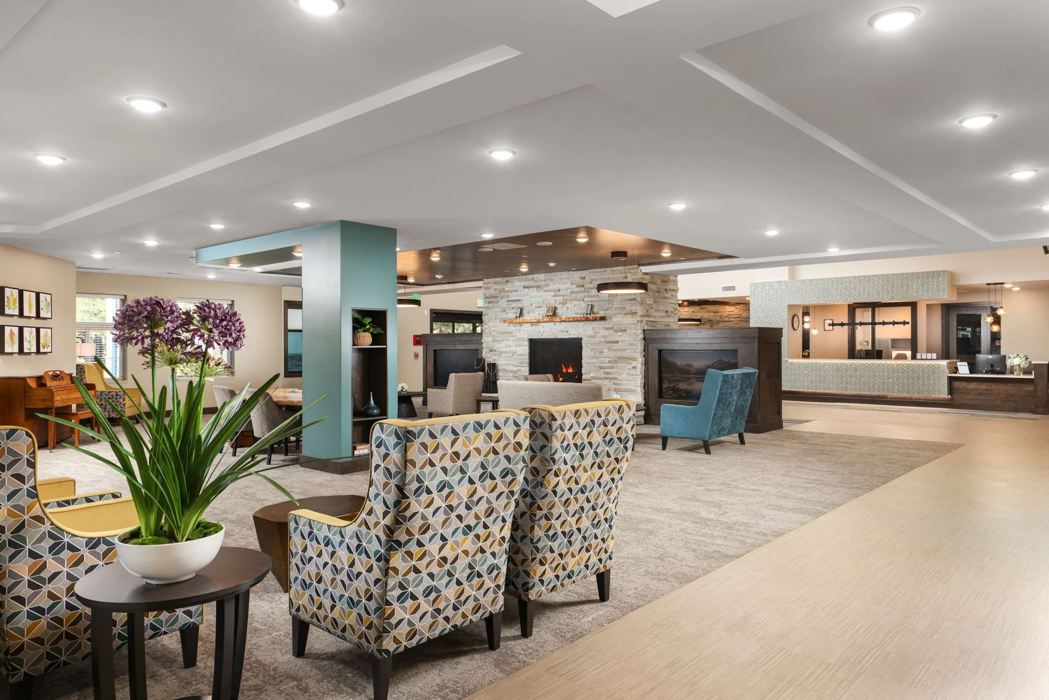 Interior of a modern lounge or lobby area with patterned chairs, potted plant, fireplace, and various seating arrangements.