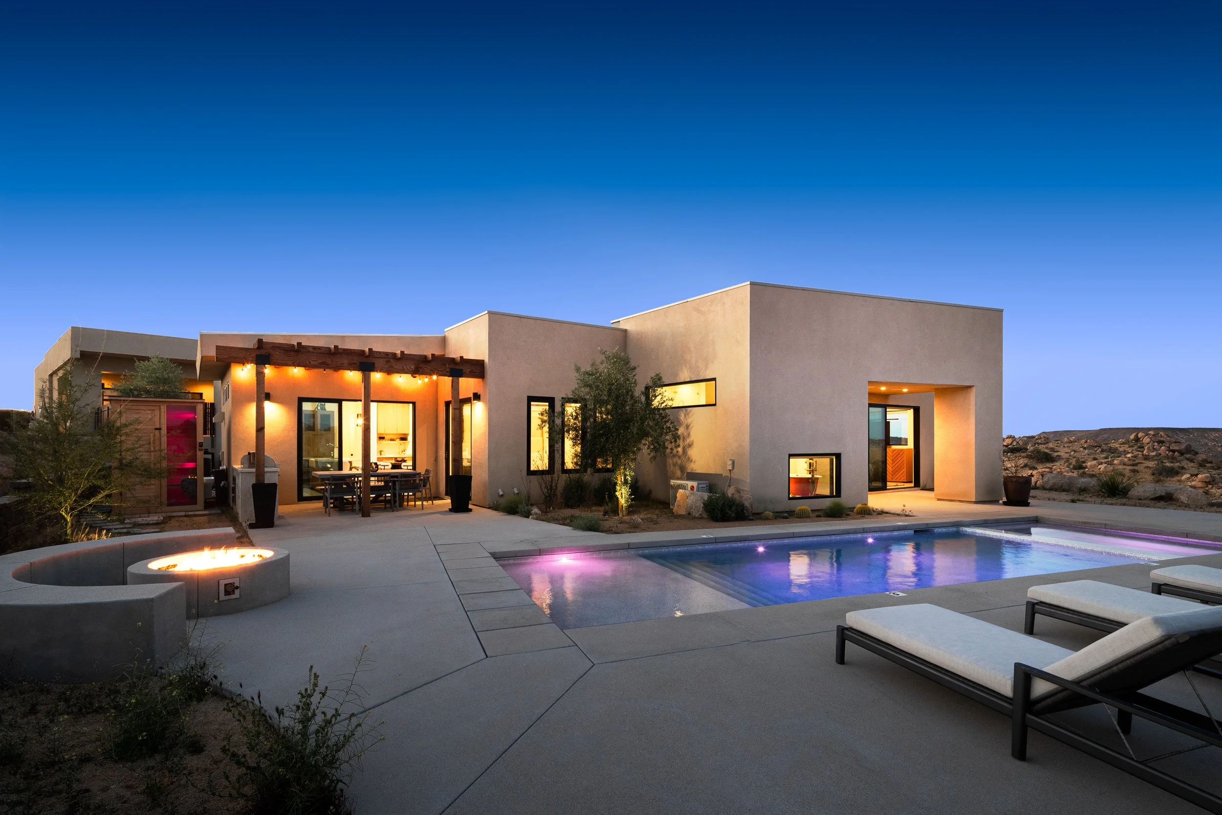 Modern house with a swimming pool and outdoor seating area at dusk under a clear blue sky.