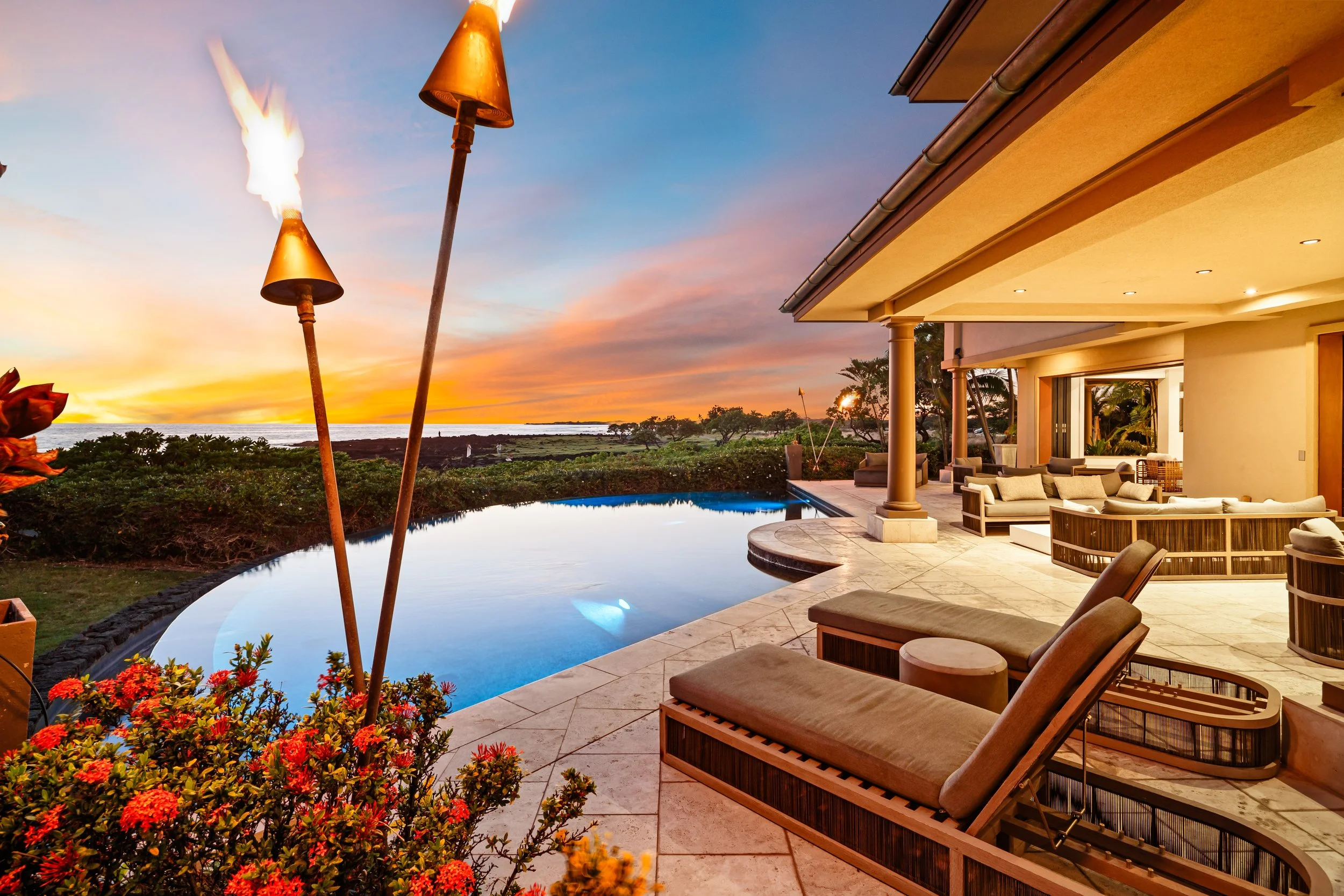 Luxury house with ocean view, outdoor pool, and patio furniture at sunset.