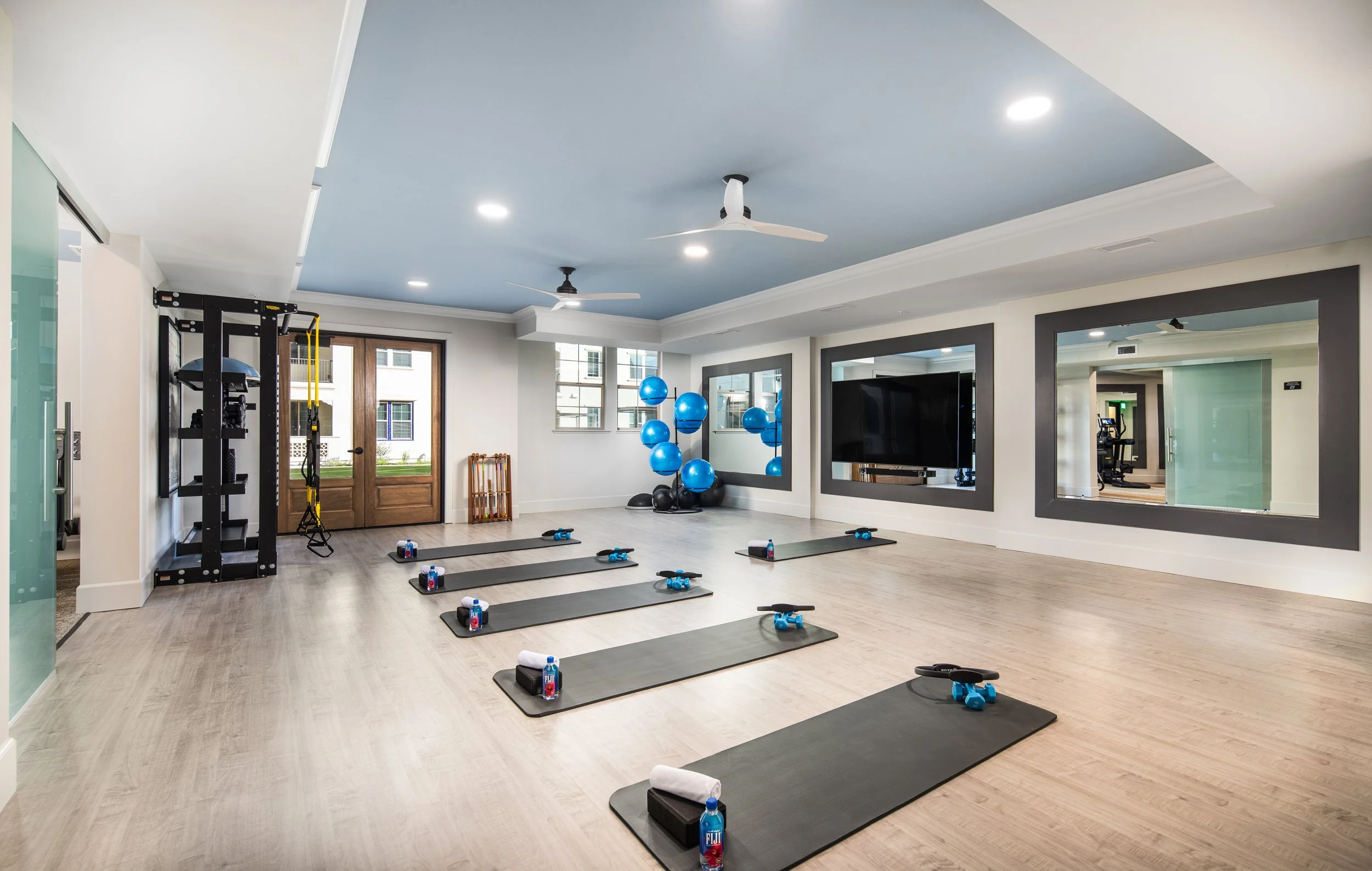 Fitness studio with yoga mats, water bottles, blue exercise balls, and mirrors on the wall.