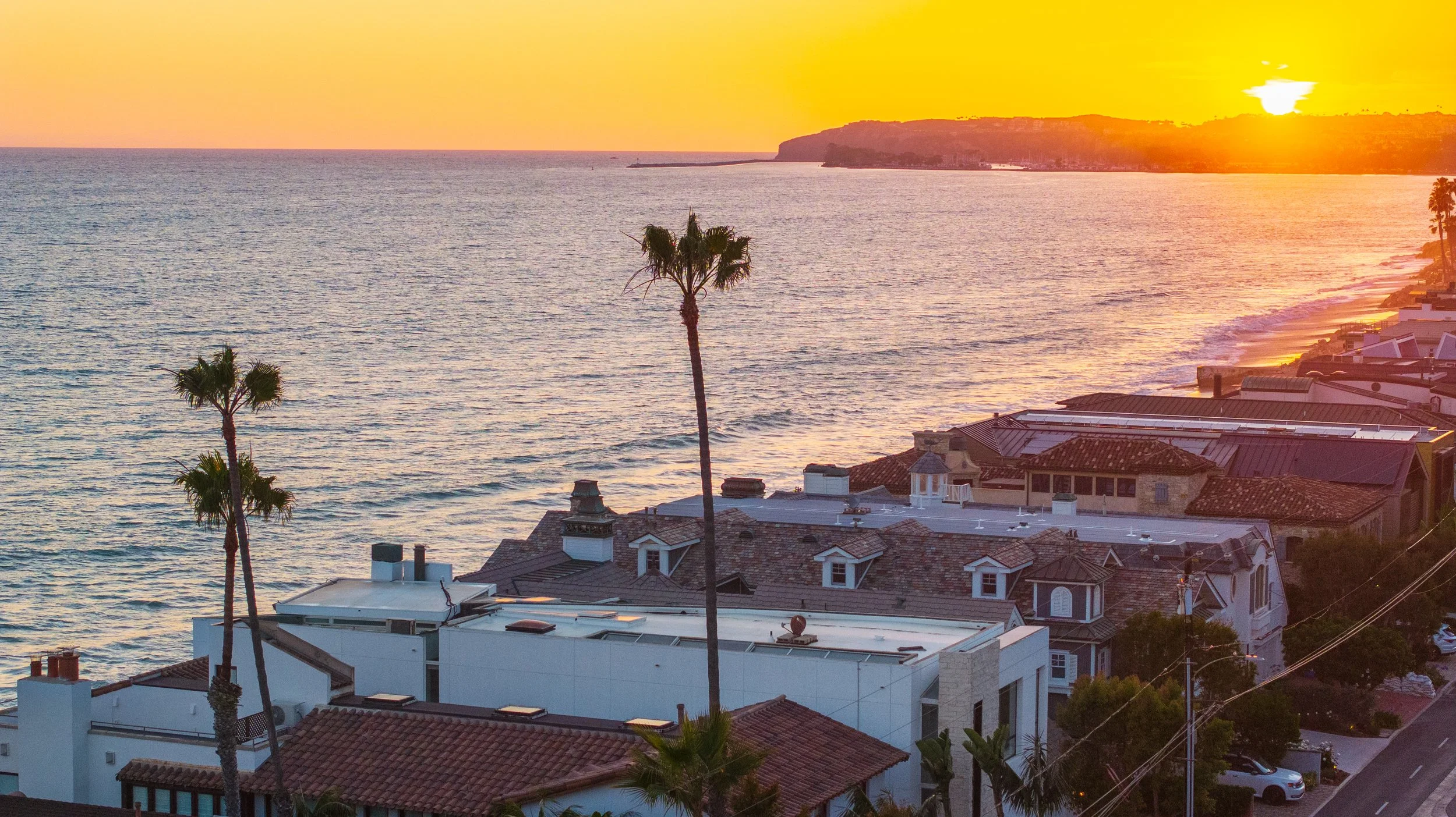 Sunset over the ocean with rooftops and palm trees in the foreground