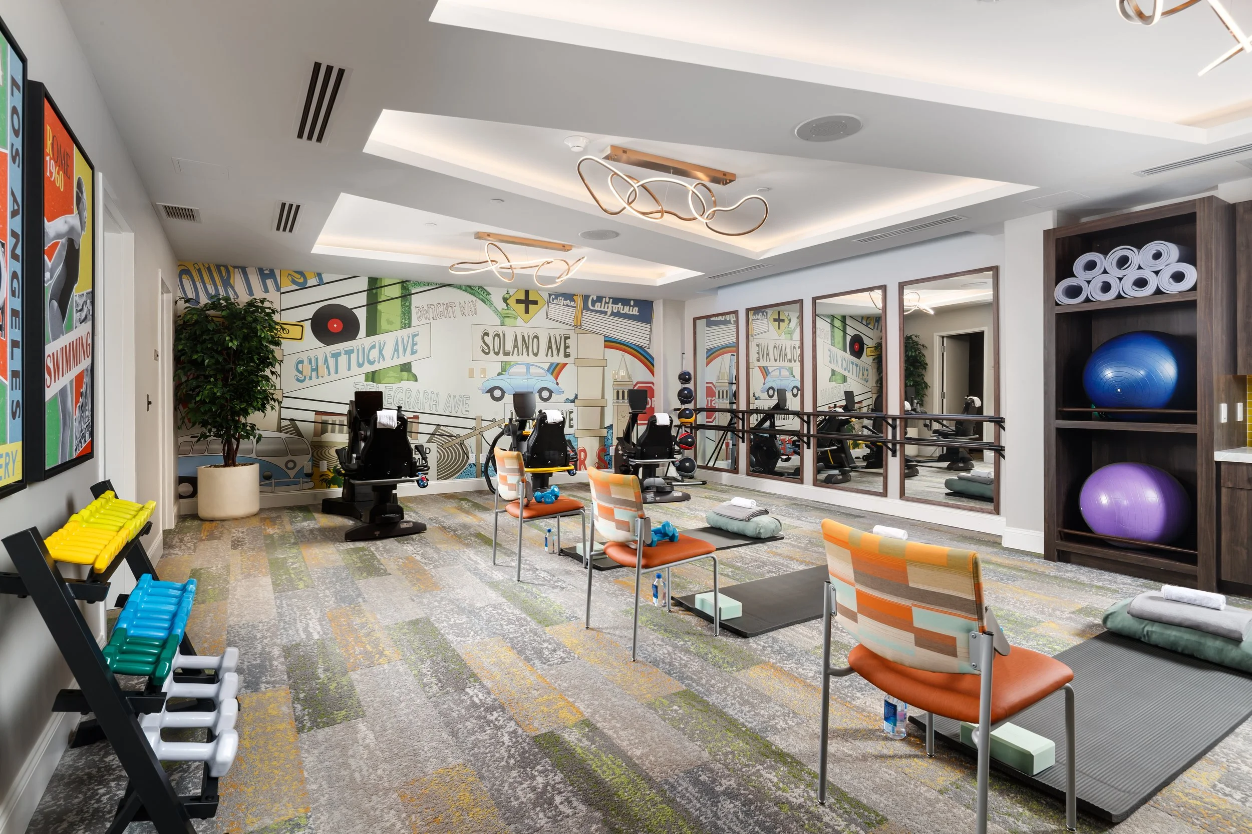 Fitness studio with exercise bikes, mats, fitness balls, and a colorful mural featuring street signs and cars.