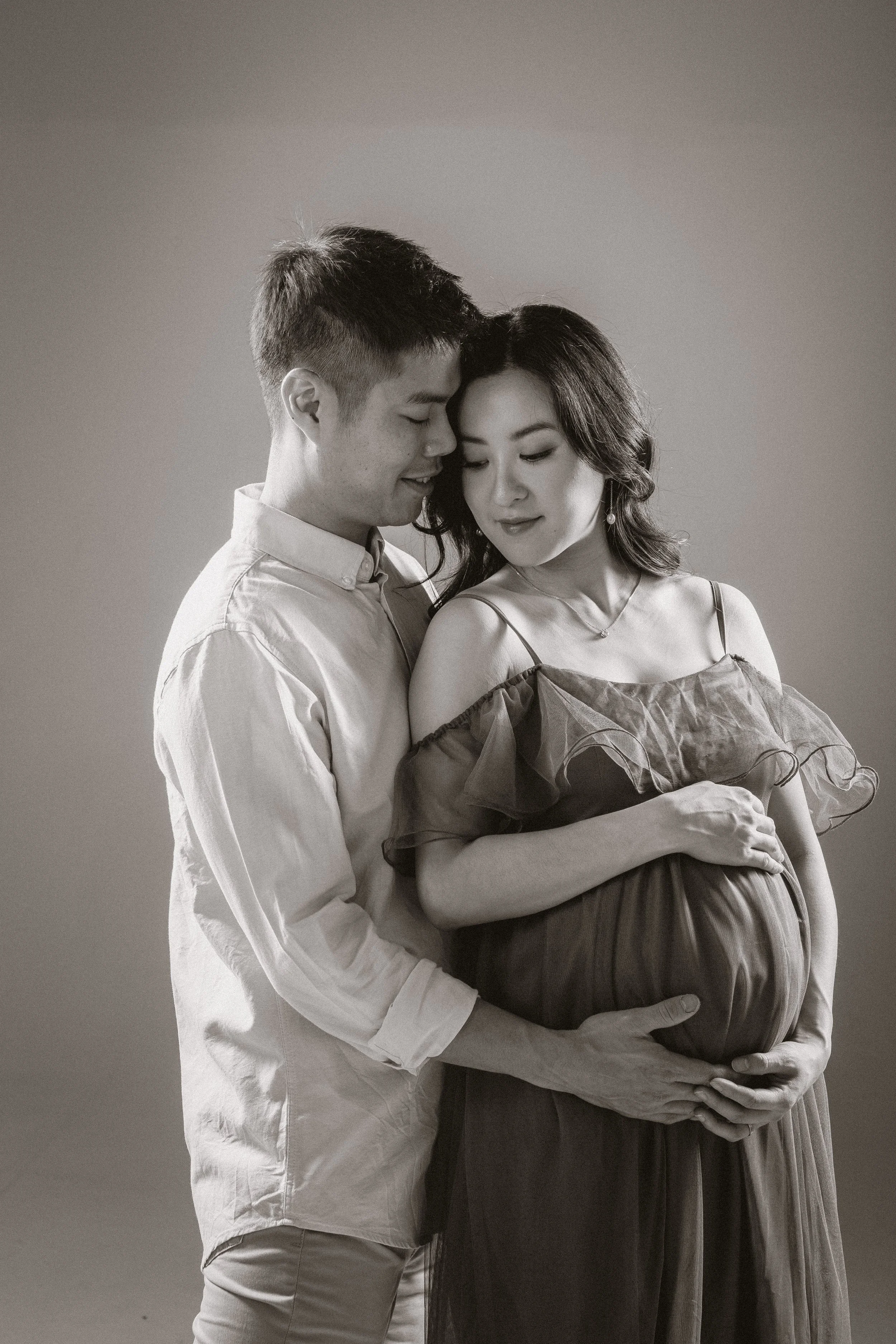 A couple with a pregnant woman embracing each other, showing love and anticipation, in a black and white portrait.