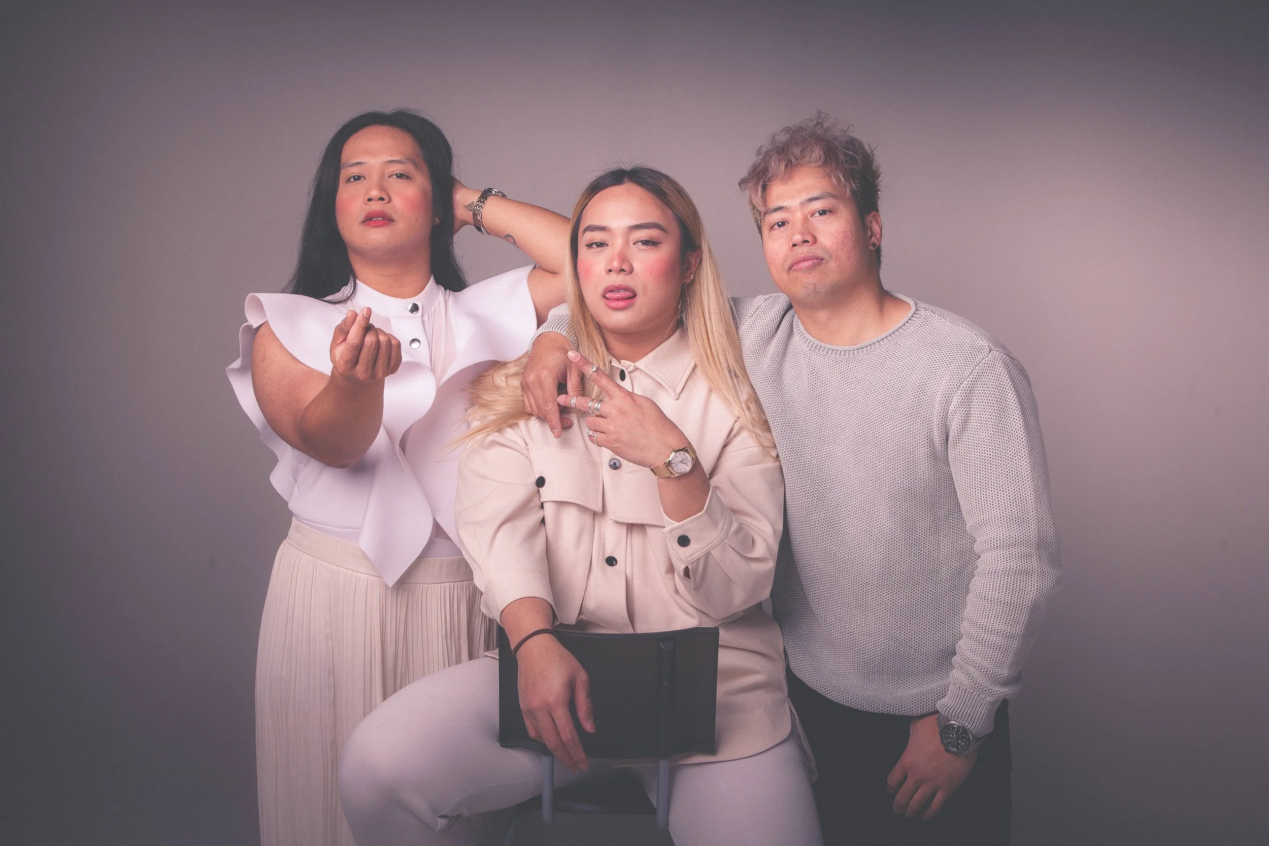 Three diverse individuals posing together against a neutral background, with confident and expressive body language and facial expressions.