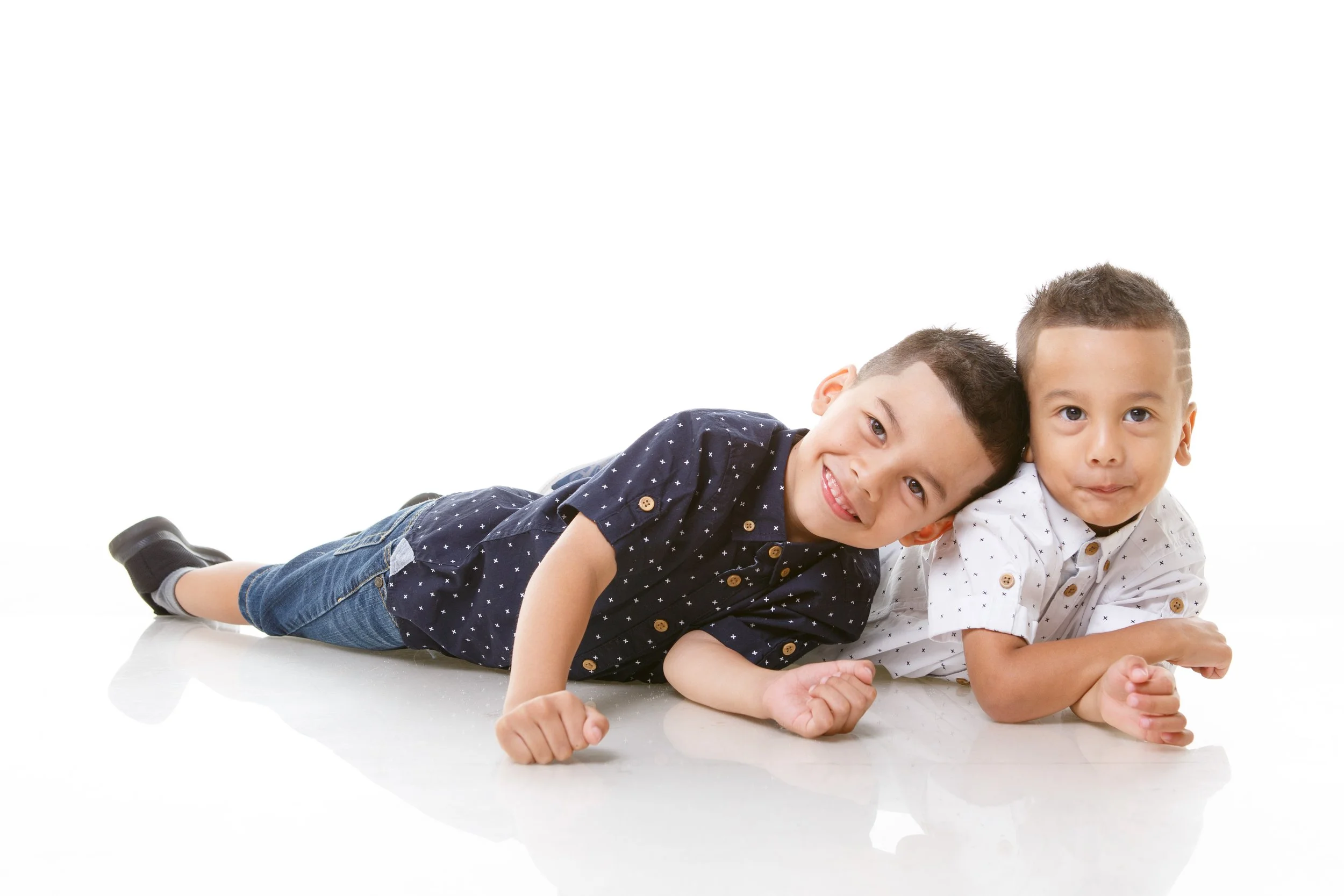 Two young boys lying on the floor, smiling and looking at the camera, with a white background.